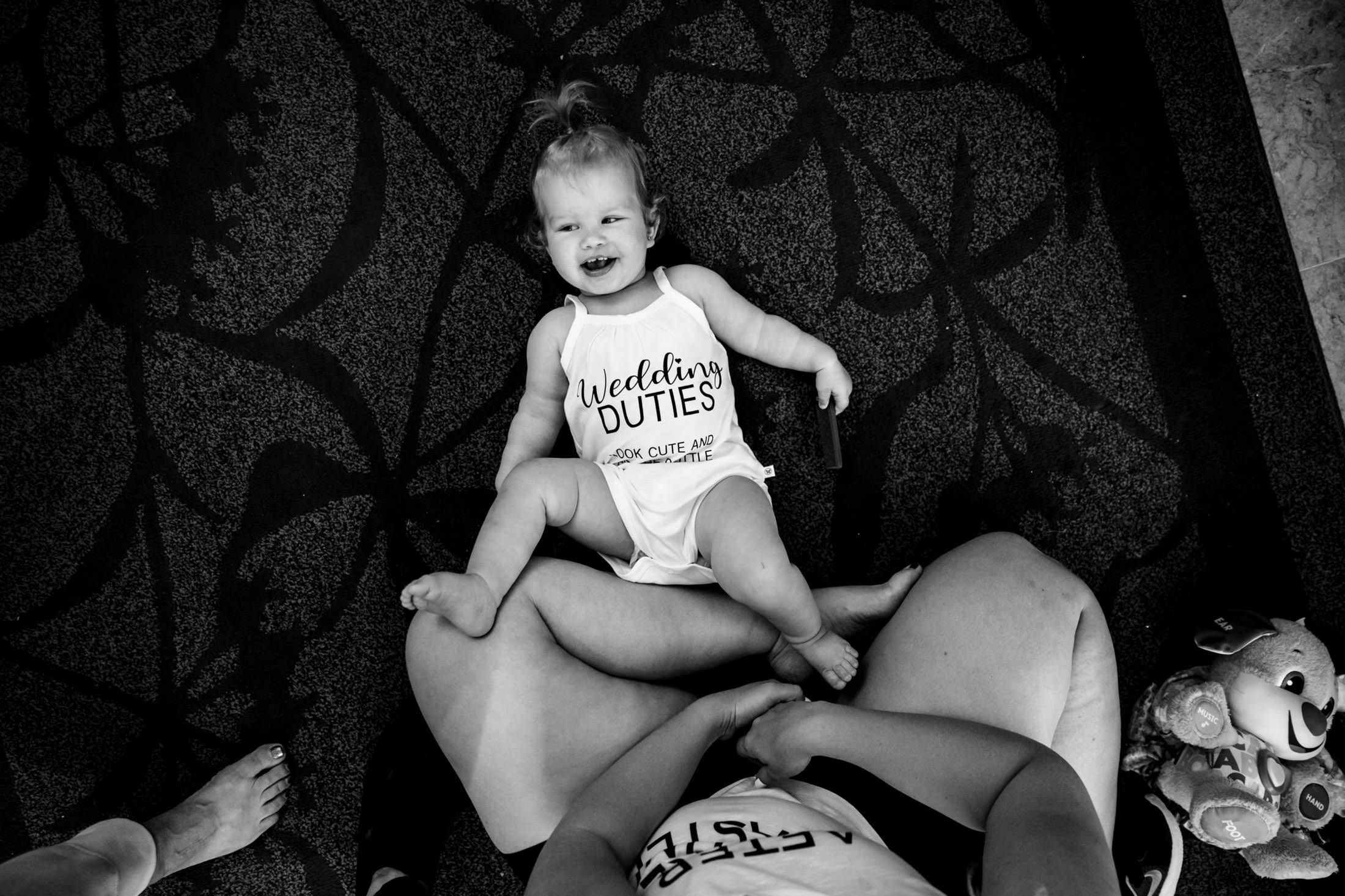 Baby in romper lies on adult's lap at Snow Lake, smiling under the wedding arch.