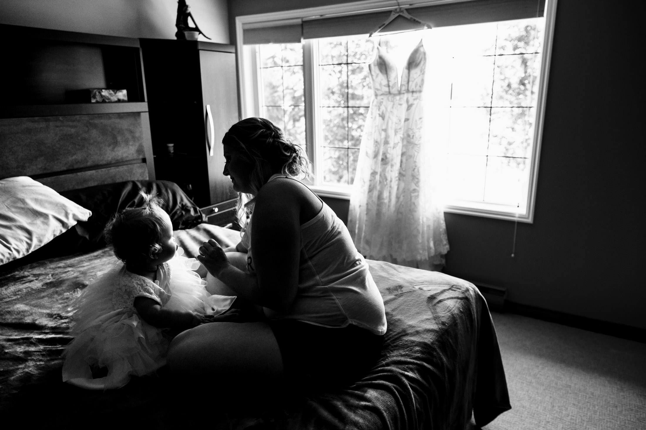 Woman on bed with toddler in dress, wedding gown by window, snow lake wedding theme.