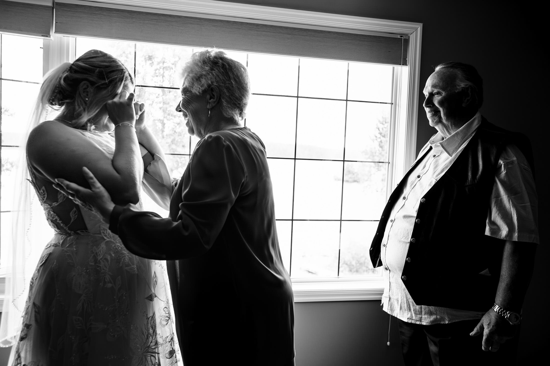 Bride crying with supportive couple at Snow Lake wedding, backlit by window.