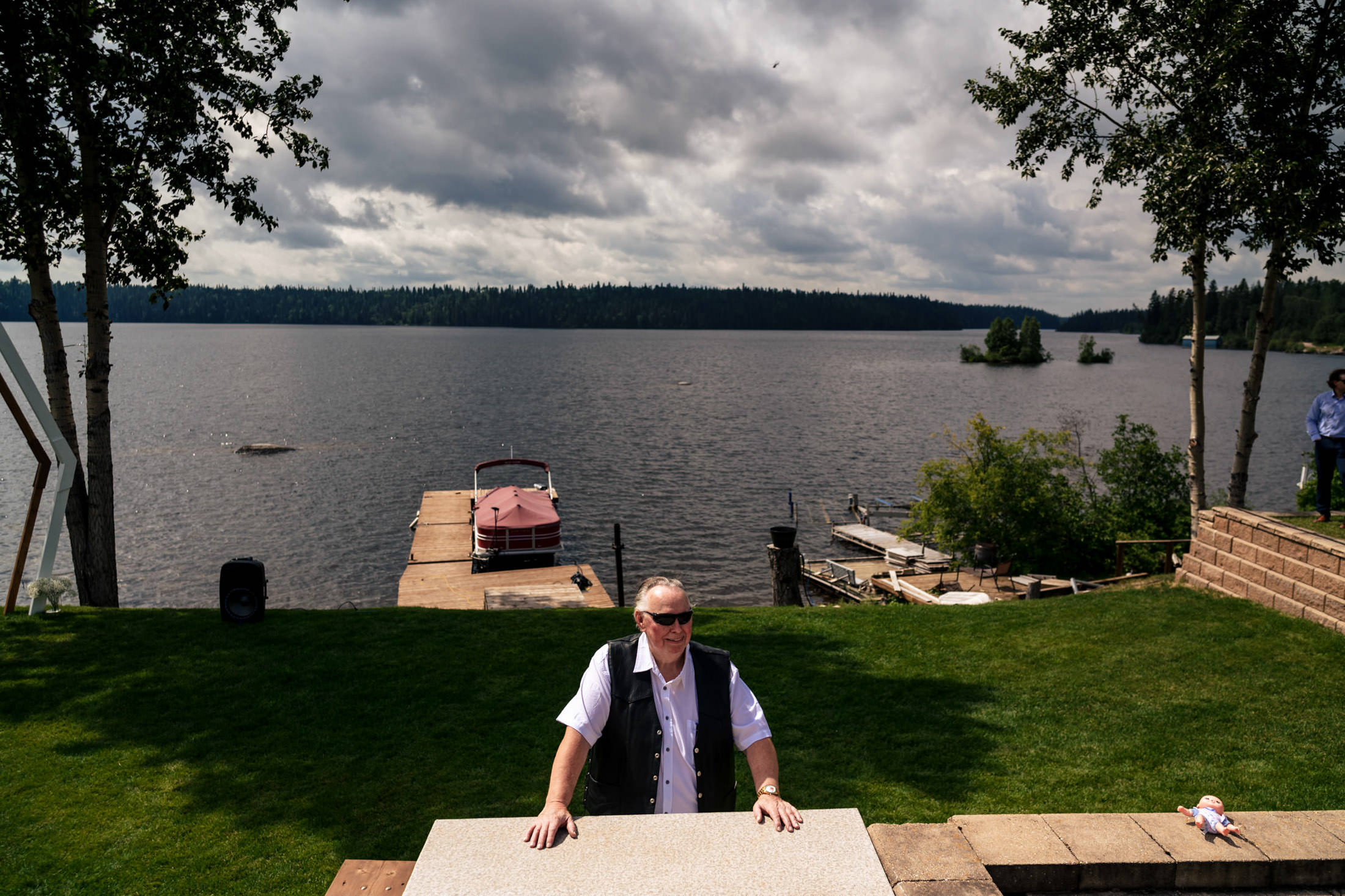 Person in sunglasses at a wedding by Snow Lake with docks and boats, under a cloudy sky.