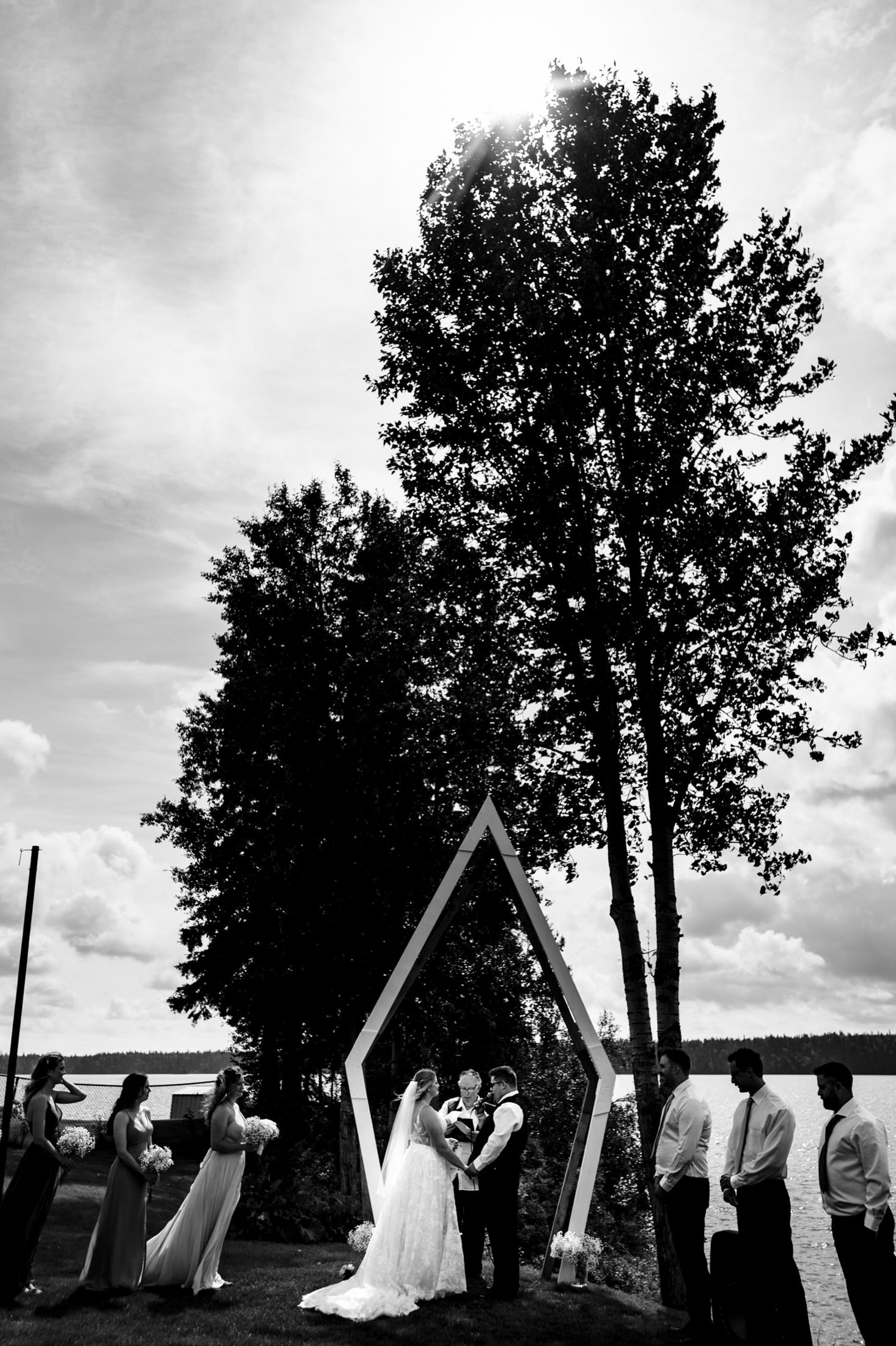 Bride and groom under a geometric arch at Snow Lake, surrounded by their wedding party.
