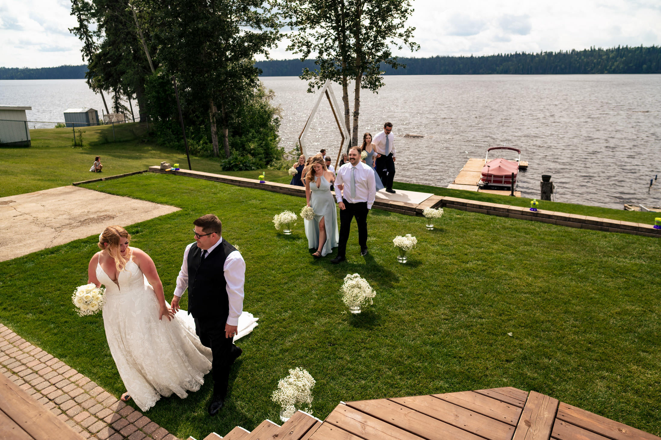 Bride and groom lead the wedding party on Snow Lake's lawn, boats and trees in the background.
