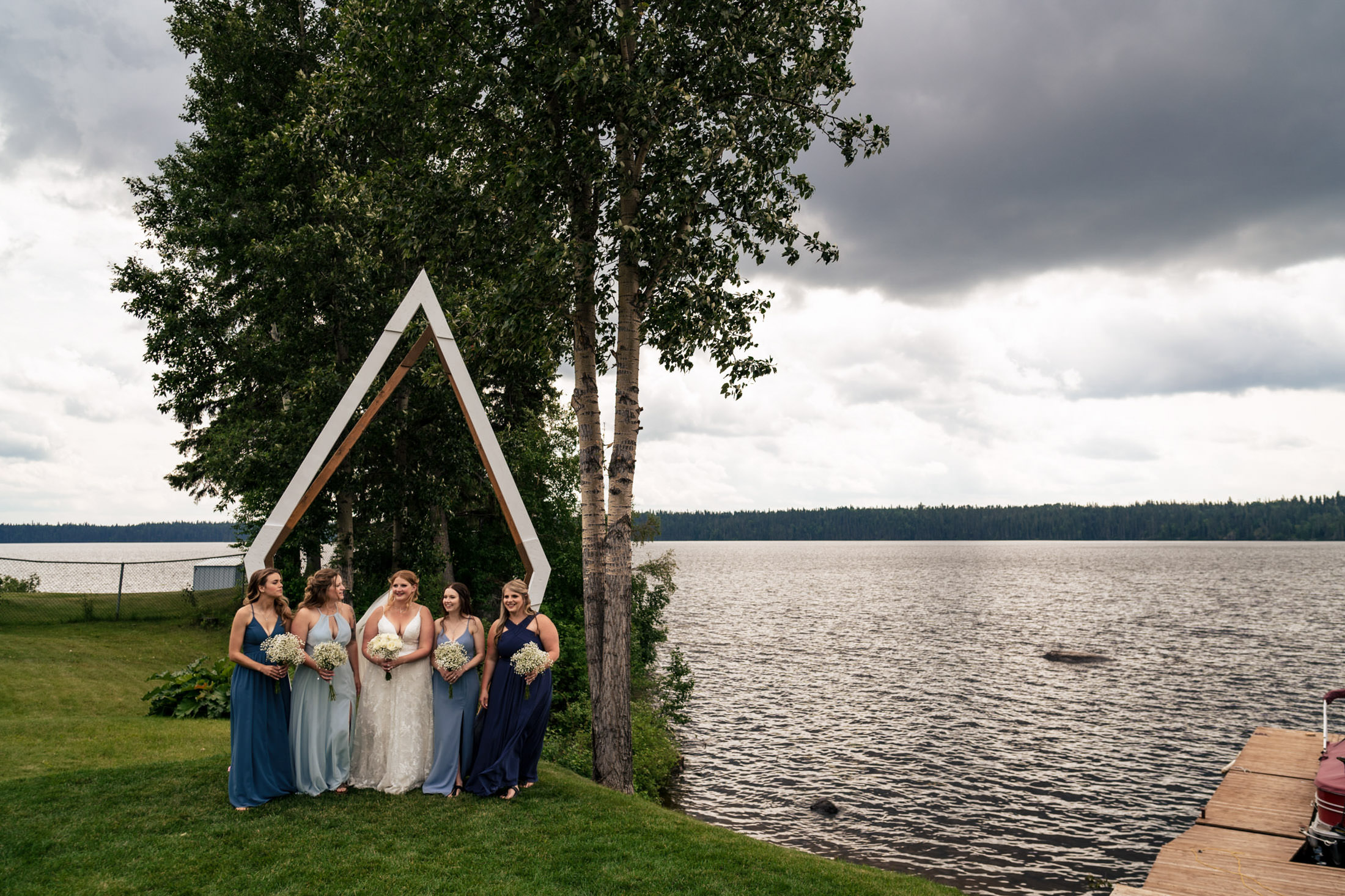 Bridal party at Snow Lake poses by a lakeside arch under cloudy skies.