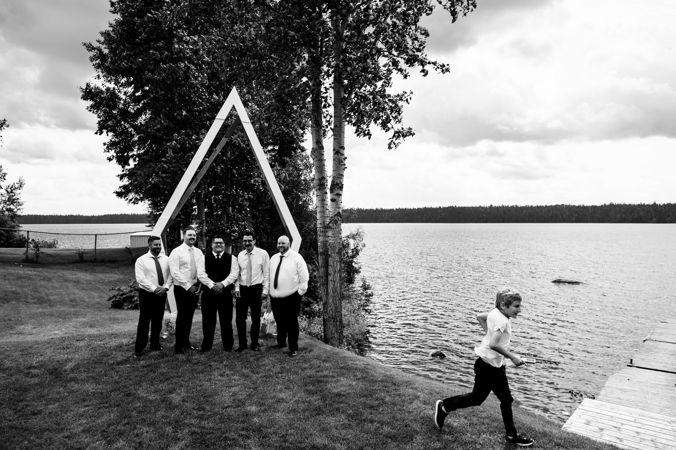 Men in formal wear by Snow Lake; a boy dashes past, hinting at a wedding nearby.