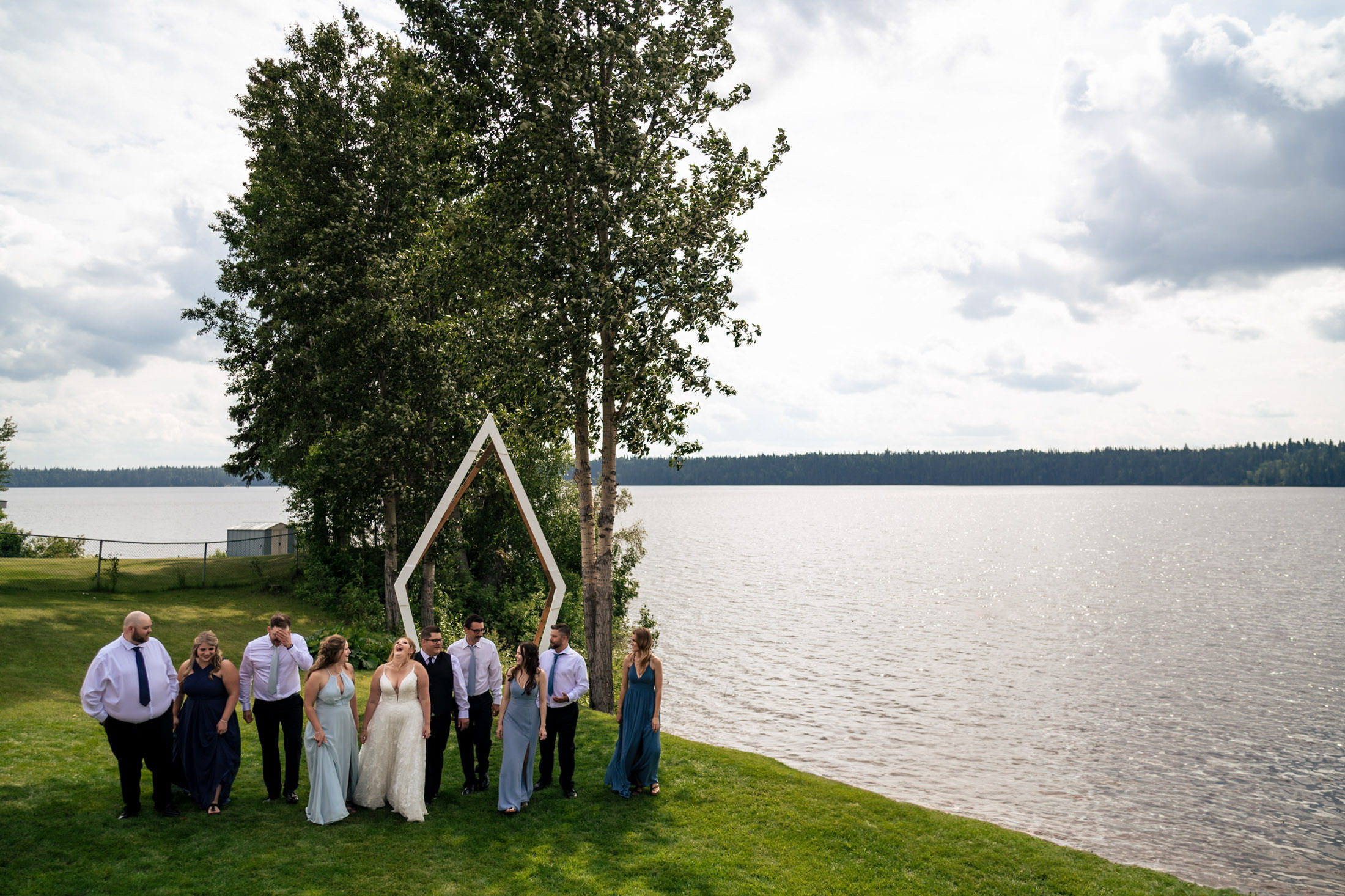 Wedding party by Snow Lake with trees and geometric arch.