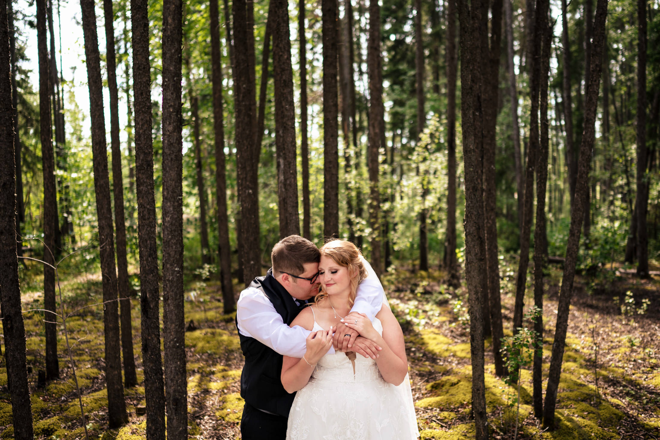Couple embracing in a forest, with sunlit trees and mossy ground at Snow Lake wedding.