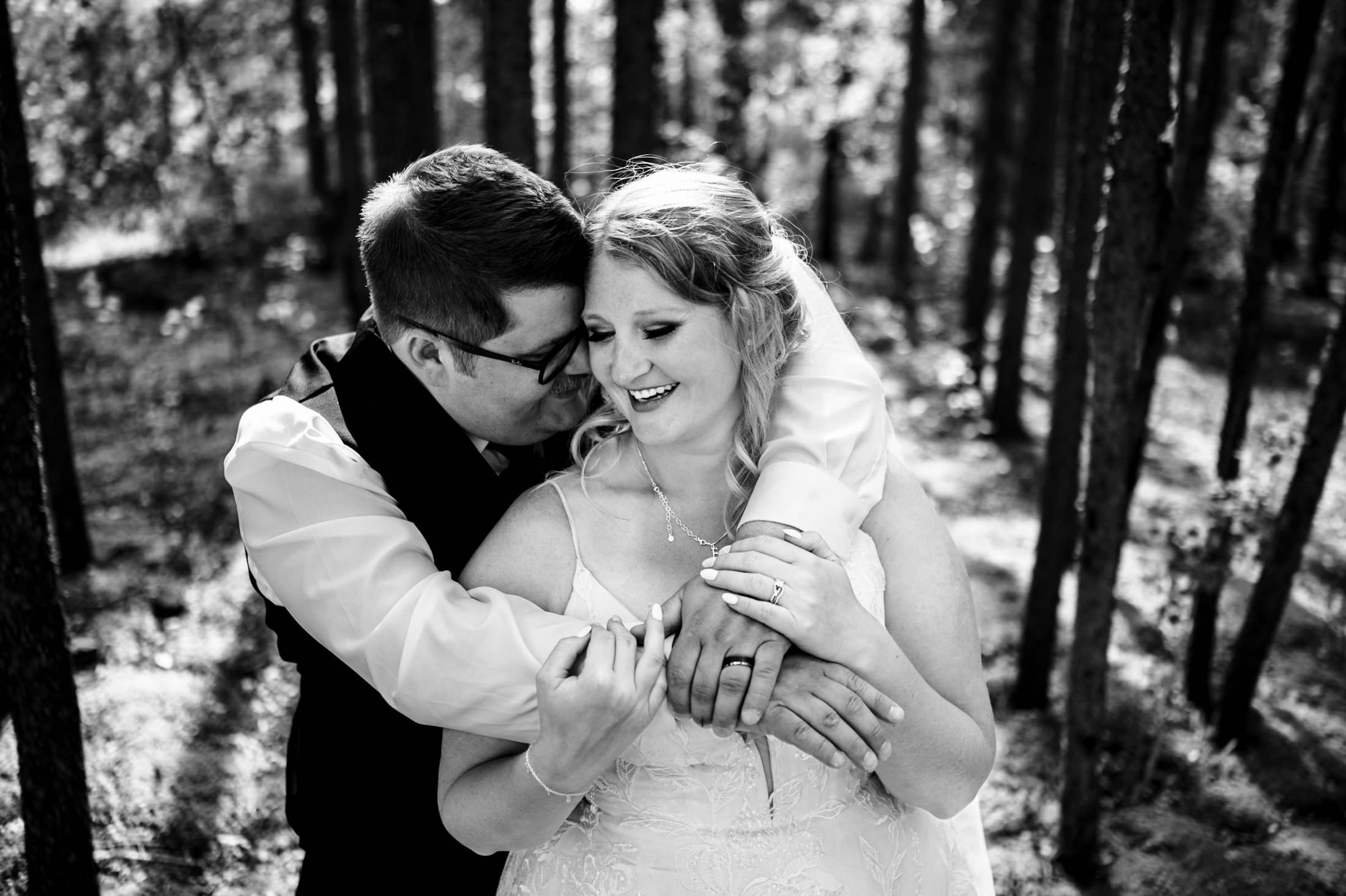 Couple joyfully hugging in Snow Lake forest, both smiling in black and white.