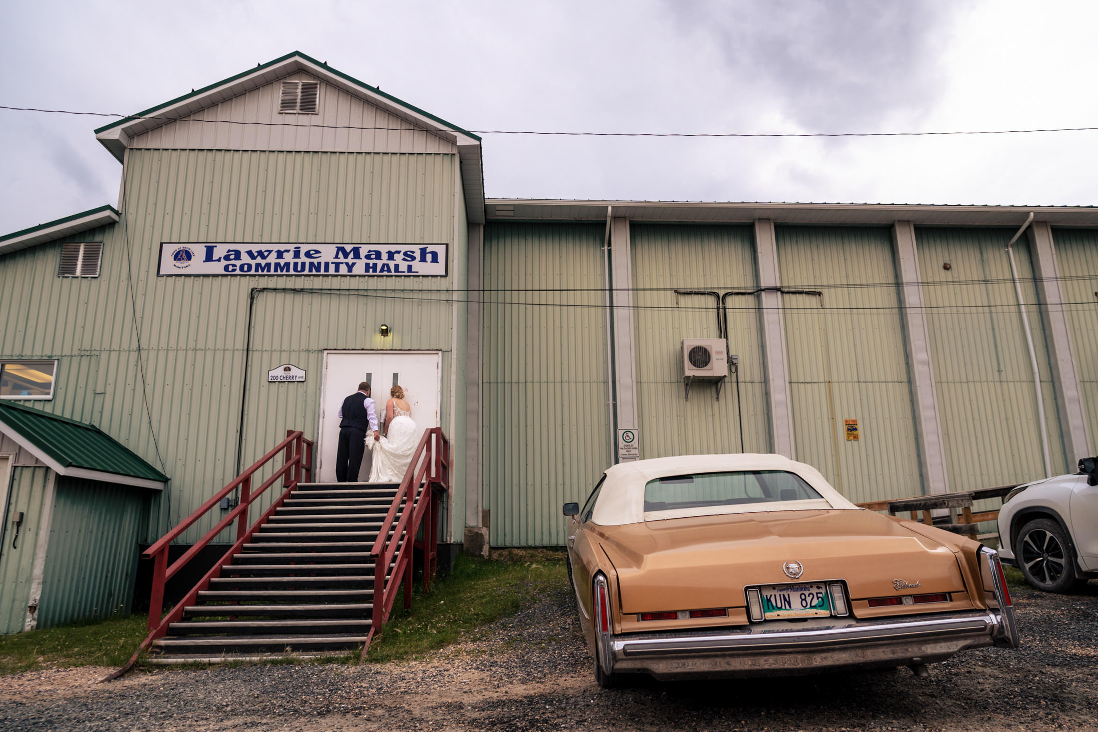 A couple enters a community hall; an old car hints at their wedding at Snow Lake.