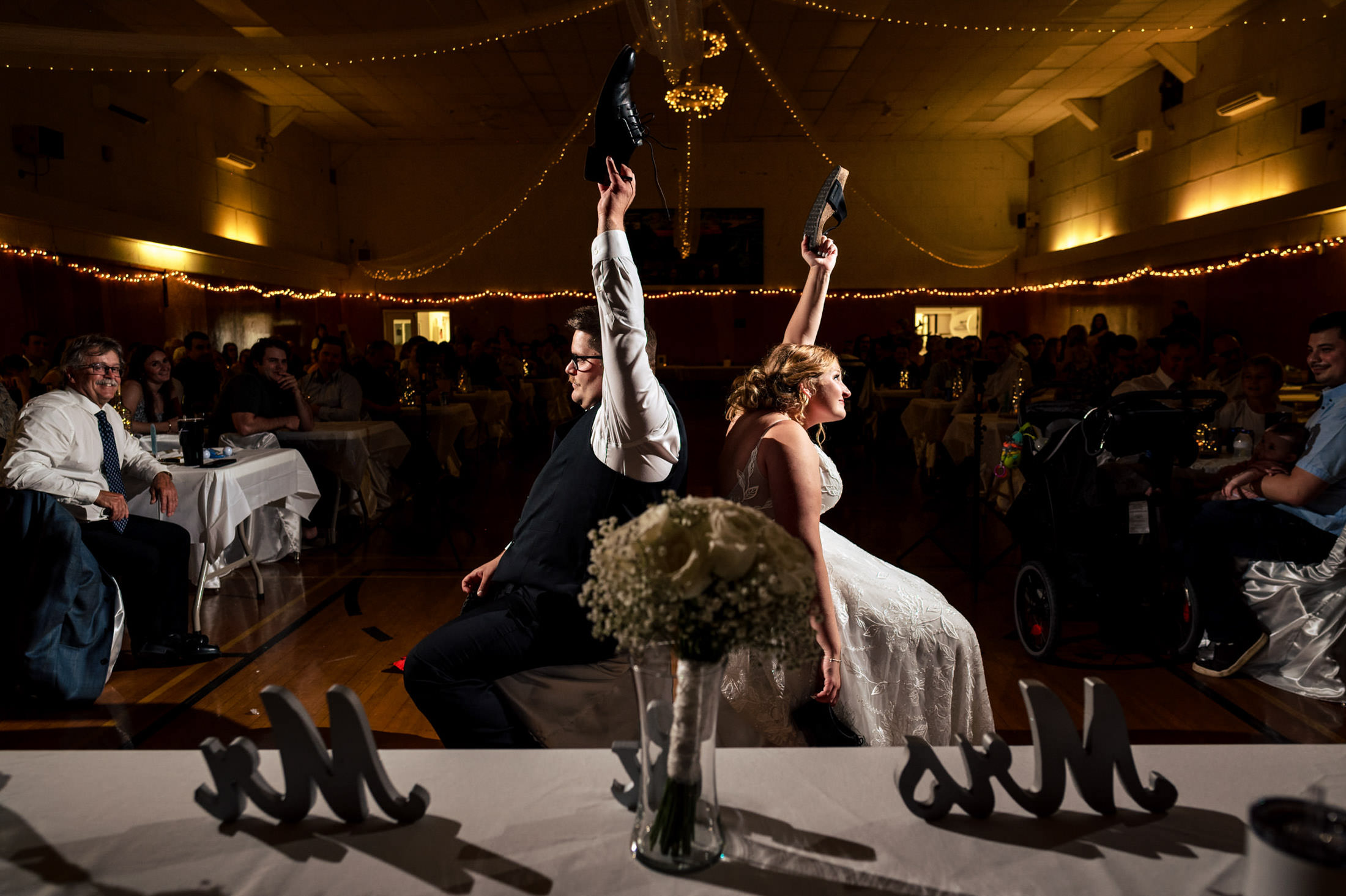 Bride and groom at Snow Lake, back-to-back, holding shoes up amid wedding guests.