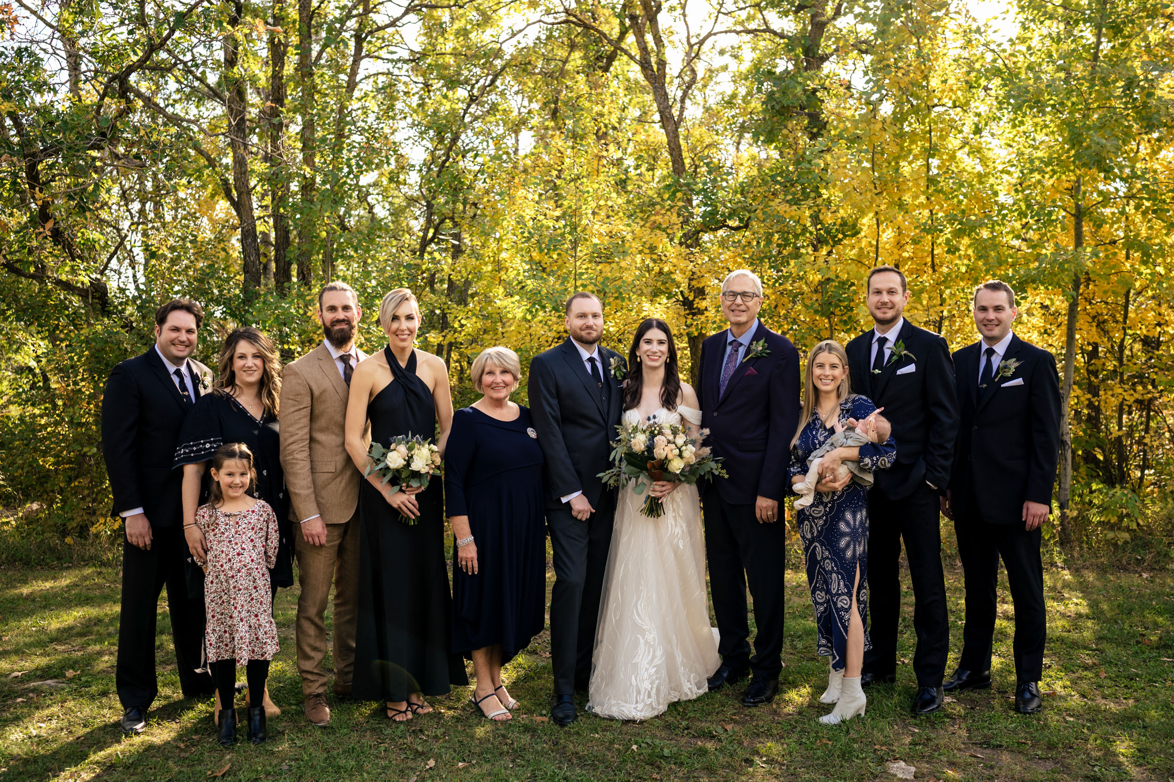 A group at a Winnipeg wedding poses outdoors with trees in the background.