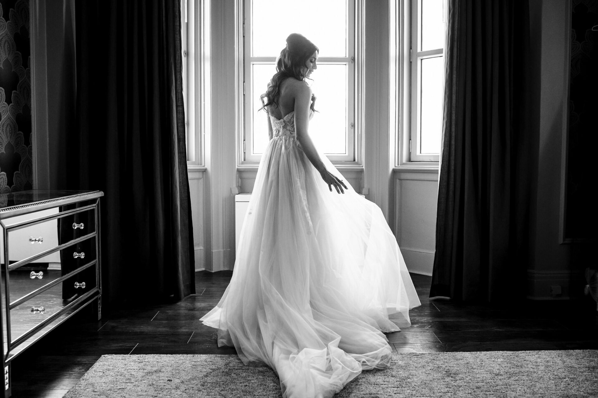 Bride in a flowing gown stands by windows, the best Winnipeg wedding photo in natural light.
