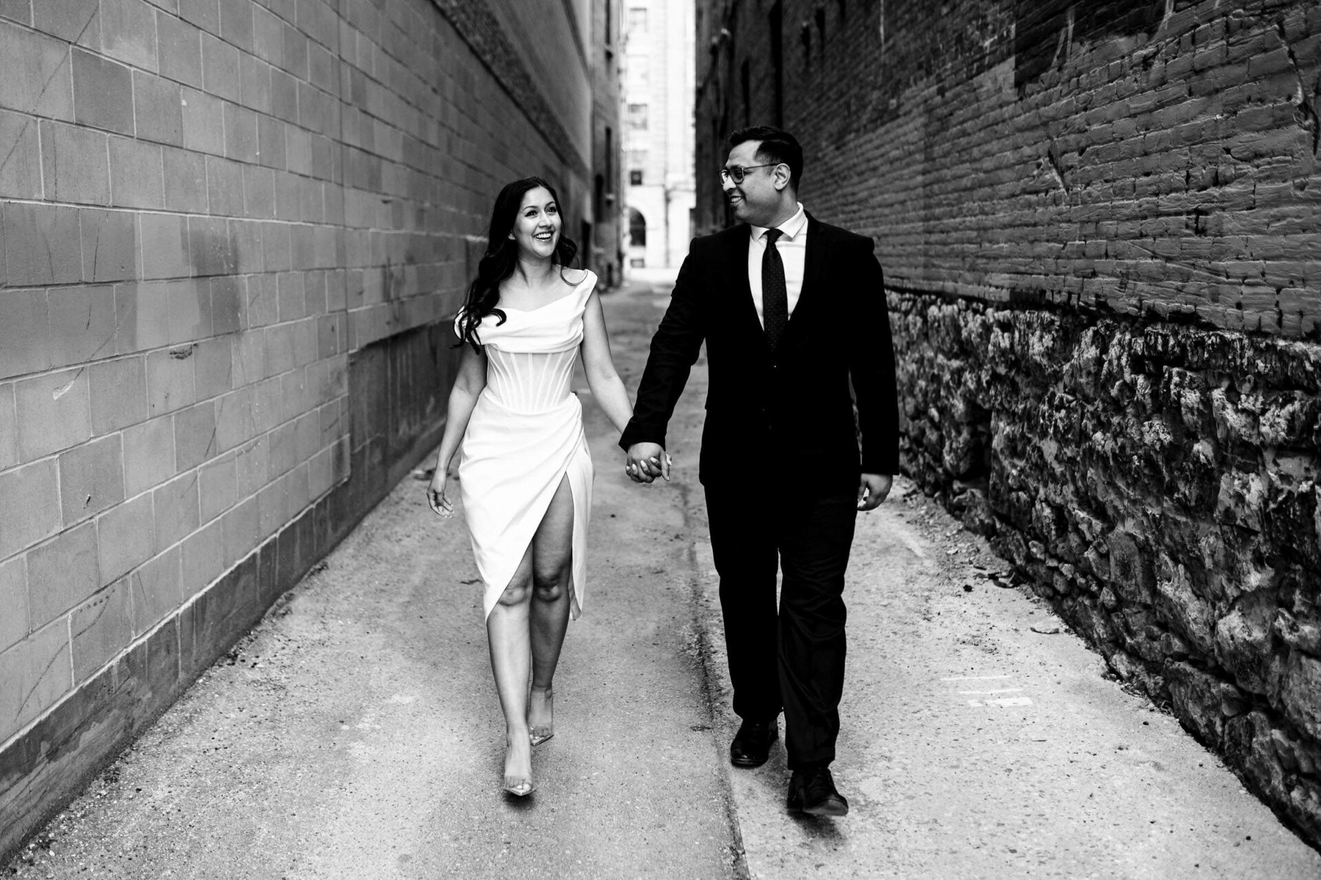 Couple holding hands in an urban alley, smiling; best Winnipeg wedding photos captured.