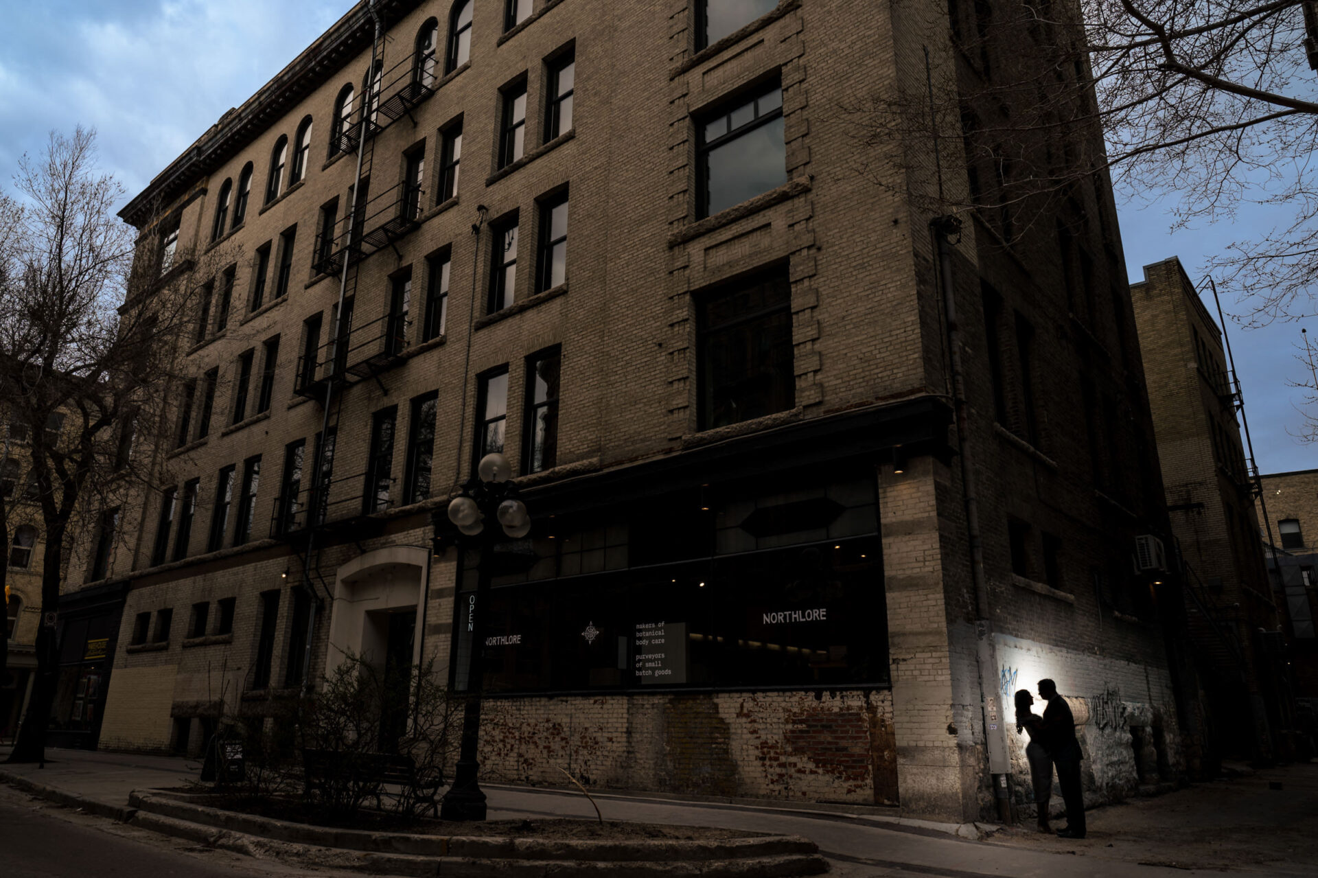 A couple embracing at dusk, capturing the best Winnipeg wedding photos by a brick building.