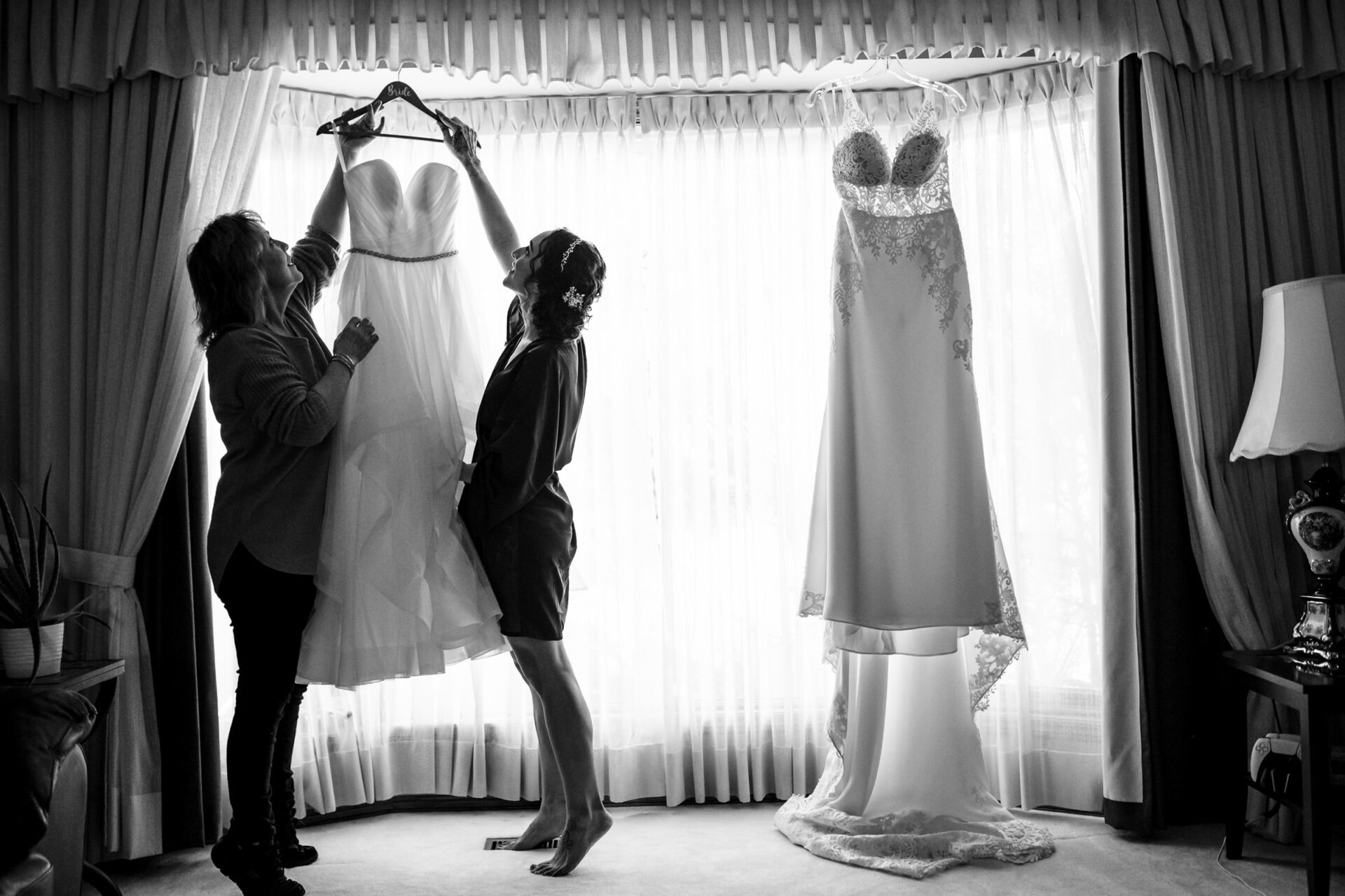 Two people hold a wedding dress; another by the window, a best Winnipeg wedding photo.