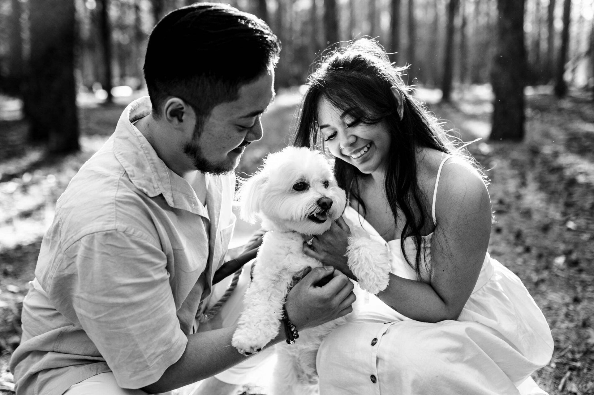 Couple grinning at a fluffy dog under sunny trees, perfect for best Winnipeg wedding photos.