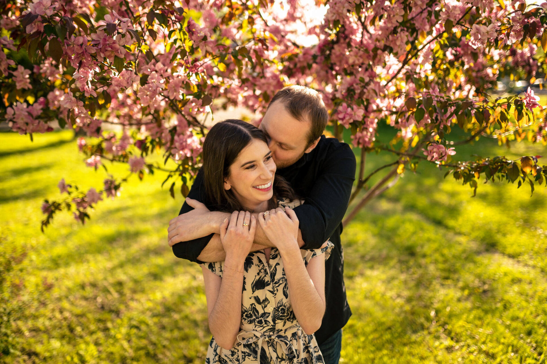 Couple embracing under blooming tree, shadows on grass—best Winnipeg wedding moment.