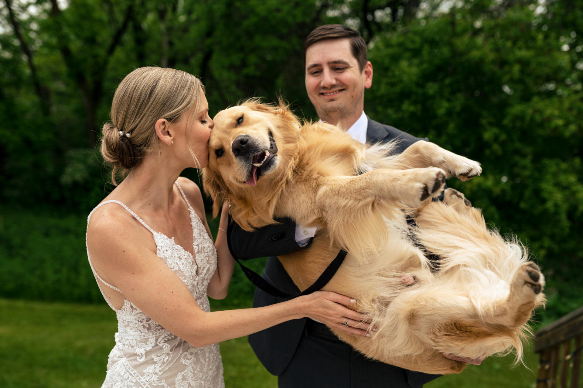 Bride and groom in Winnipeg holding a happy dog outdoors for the best wedding photo.