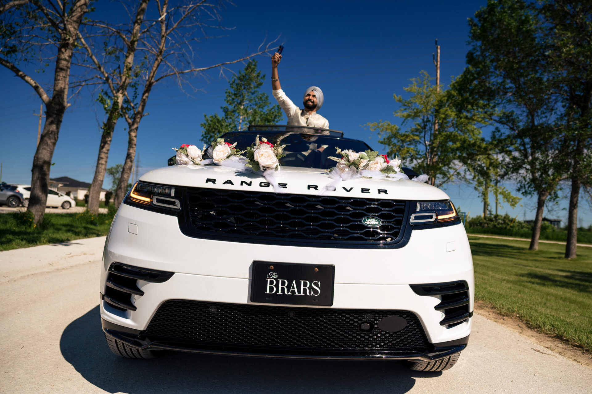 Man celebrating in sunroof of decorated Range Rover on a sunny day. Best Winnipeg wedding photo.