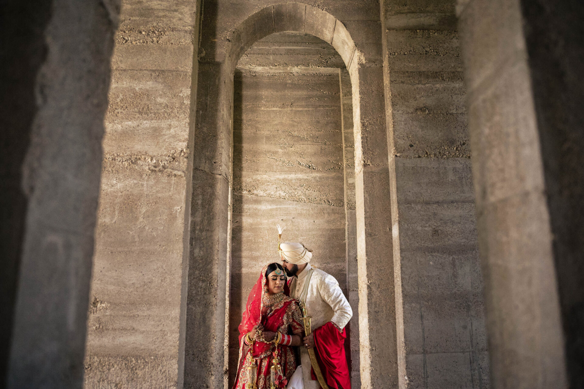 Couple in traditional attire captured under a stone archway, best Winnipeg wedding photos.