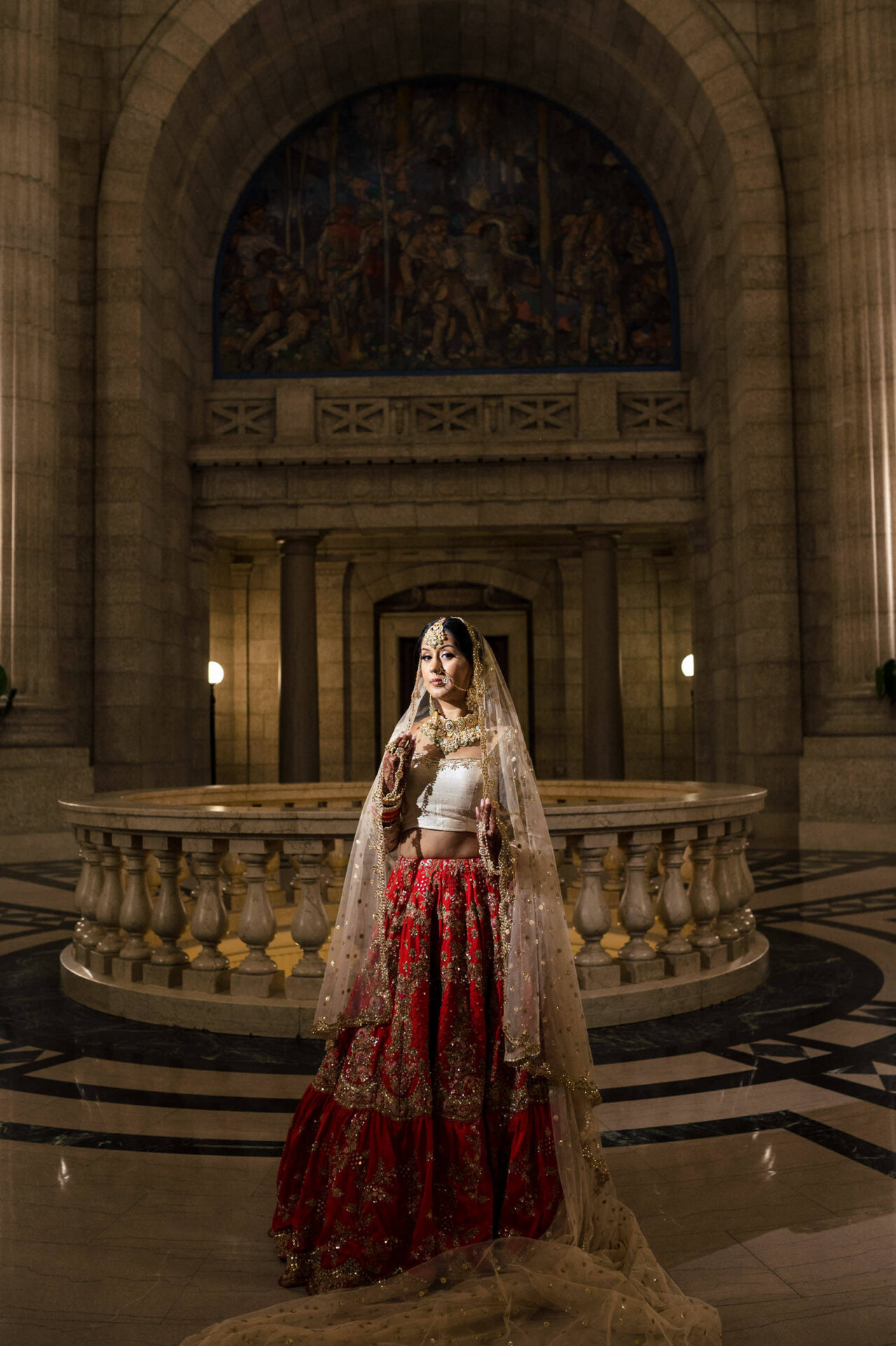 Bride in red and gold attire in grand hall, among the best Winnipeg wedding photos.
