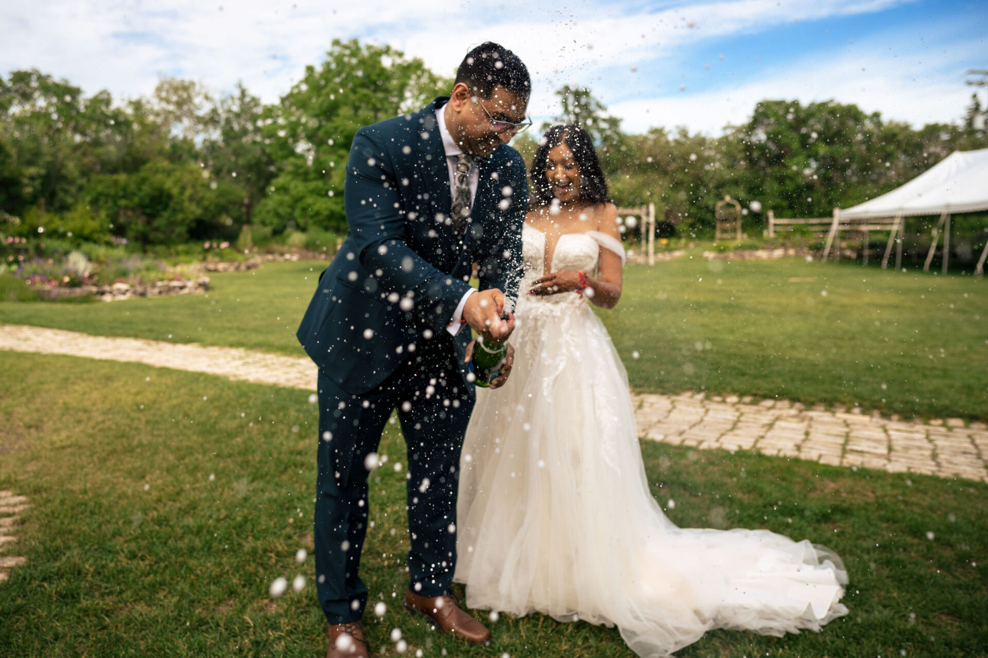 Best Winnipeg Wedding Photos: Couple outdoors, man opens champagne, woman in wedding dress smiles.