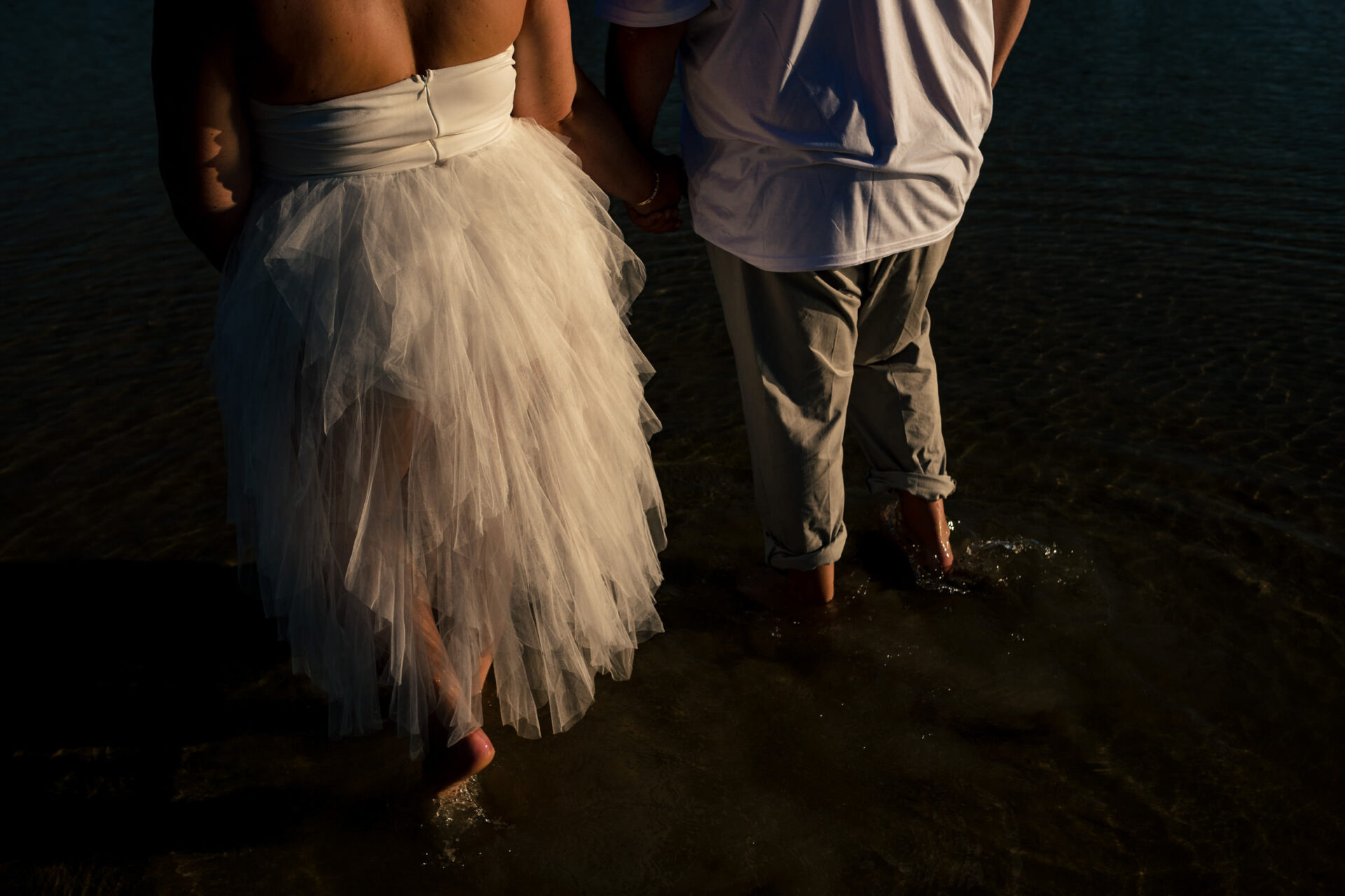 Couple holding hands, in wedding attire, captured in shallow water - best Winnipeg moment.