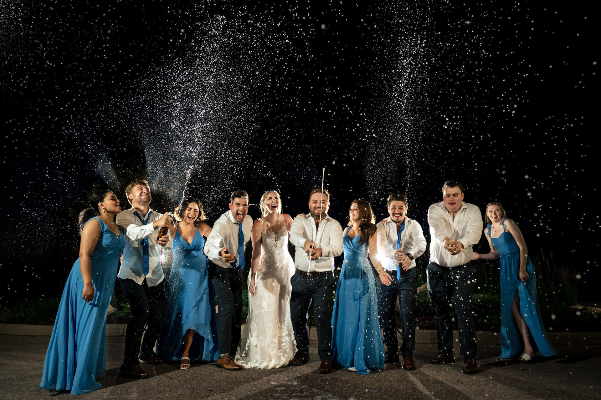 Winnipeg wedding party celebrates, spraying champagne with joy at night.