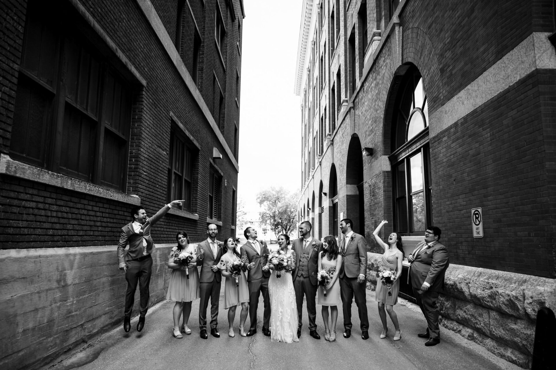Best Winnipeg wedding photos show a party posing between tall brick buildings in black and white.