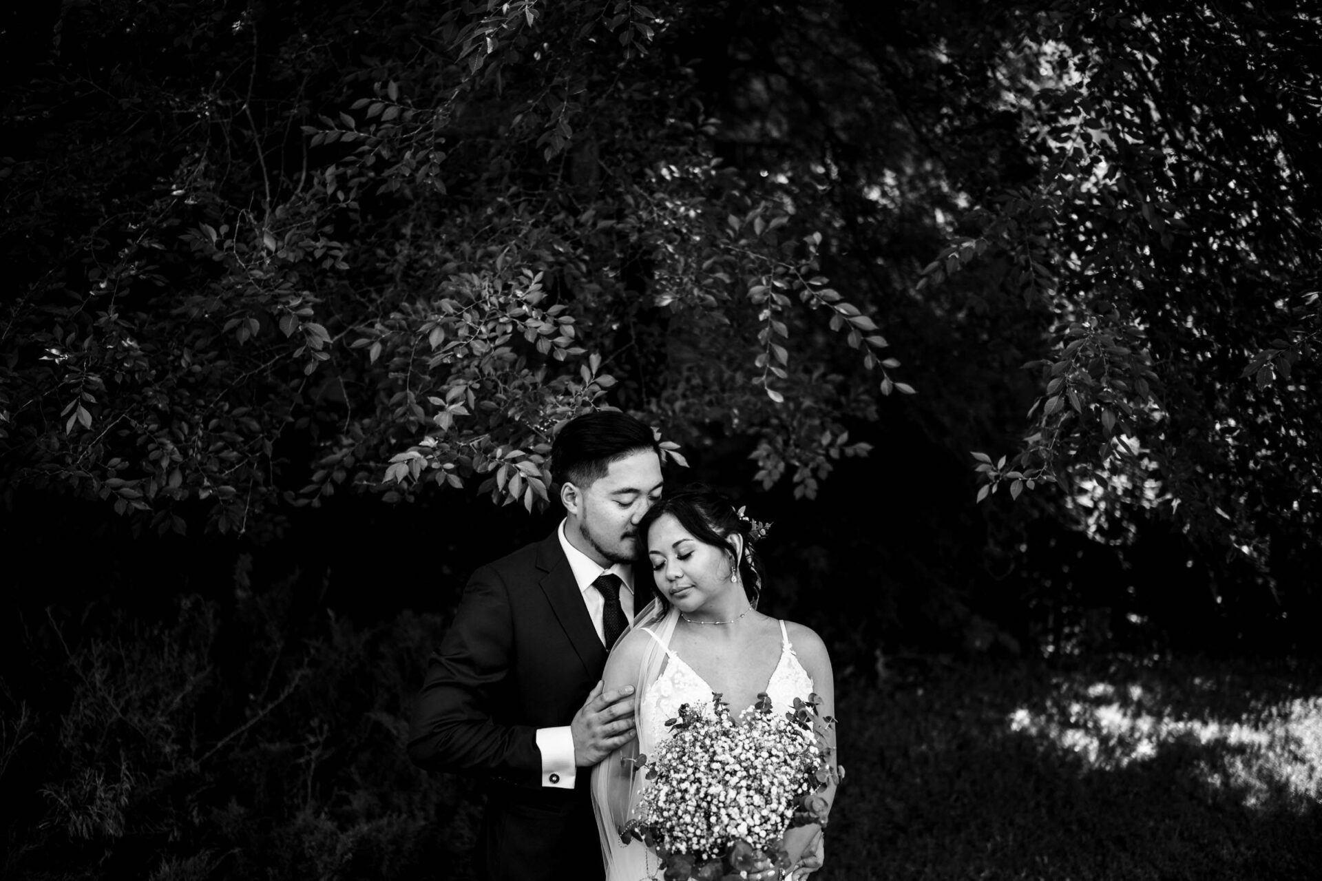 Bride and groom embrace under leafy branches in the Best Winnipeg Wedding Photos.