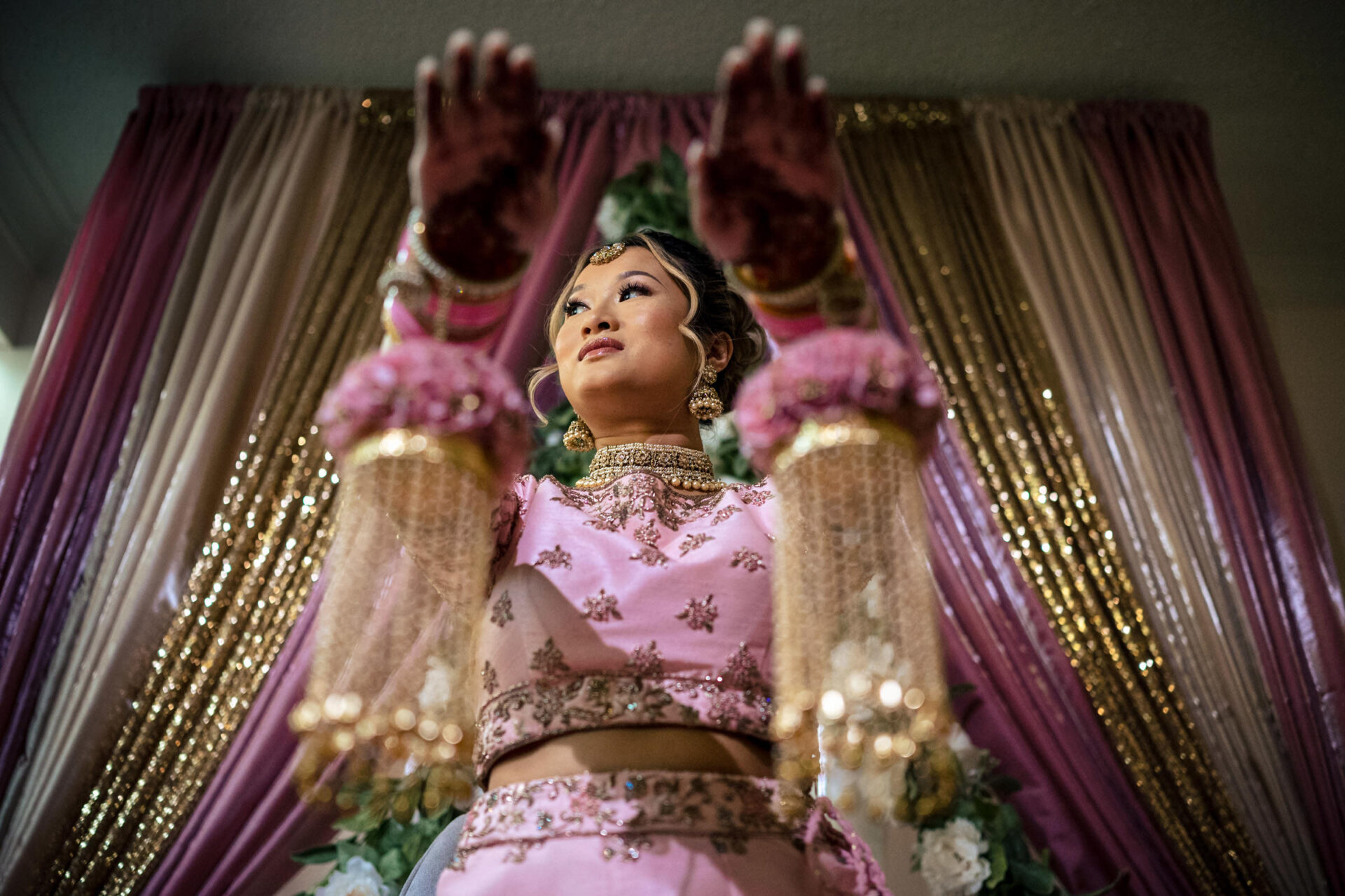 Woman in pink attire with henna, arms raised; best Winnipeg wedding photo backdrop behind.