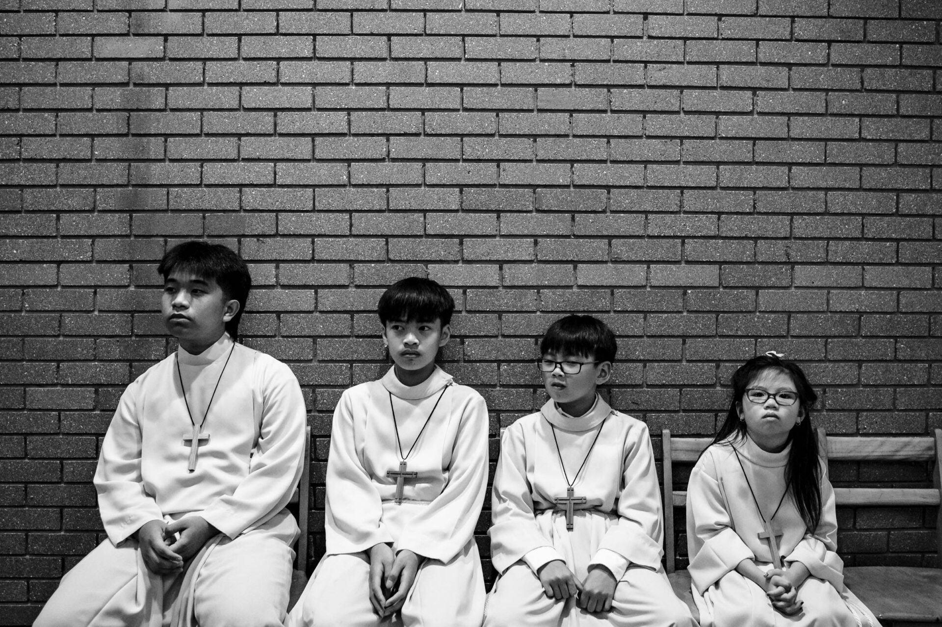Four robed children with crosses sit on a bench, a timeless black and white Winnipeg photo.