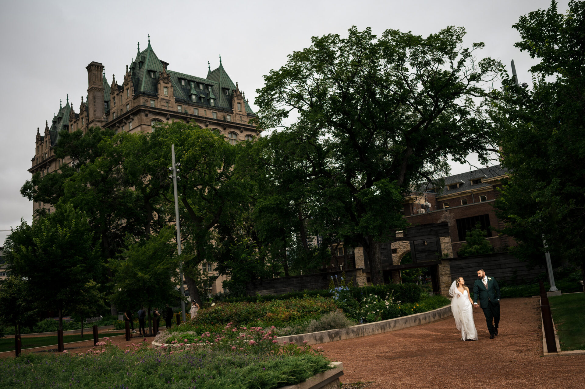 Bride and groom in garden, historic building backdrop—best Winnipeg wedding photos.