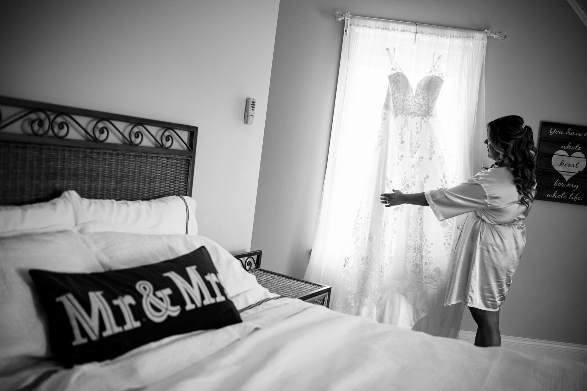 Bride in robe admiring lace wedding dress by window, captured in best Winnipeg wedding photos.