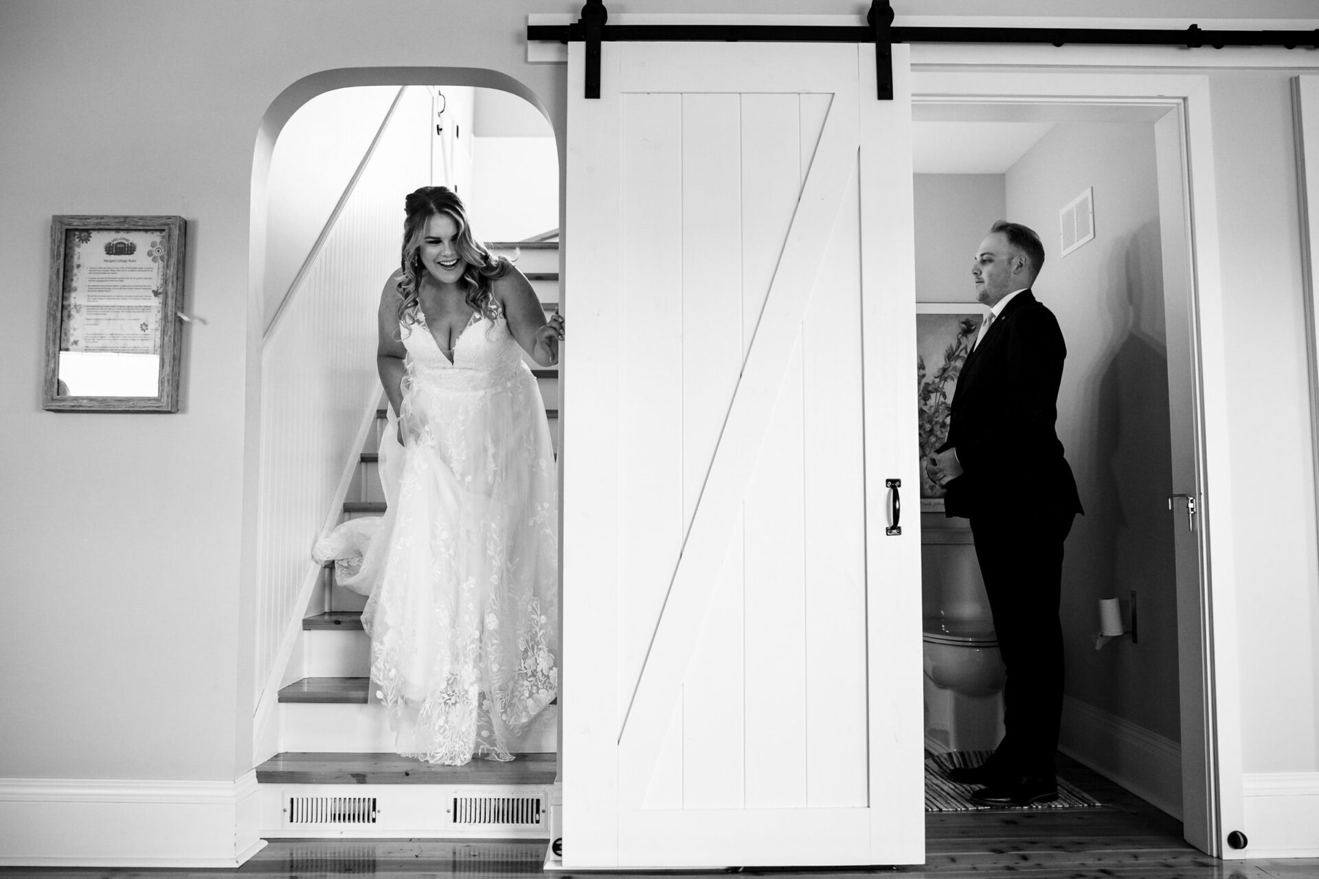 Bride descends stairs smiling, groom waits by sliding door; a top Winnipeg wedding photo.