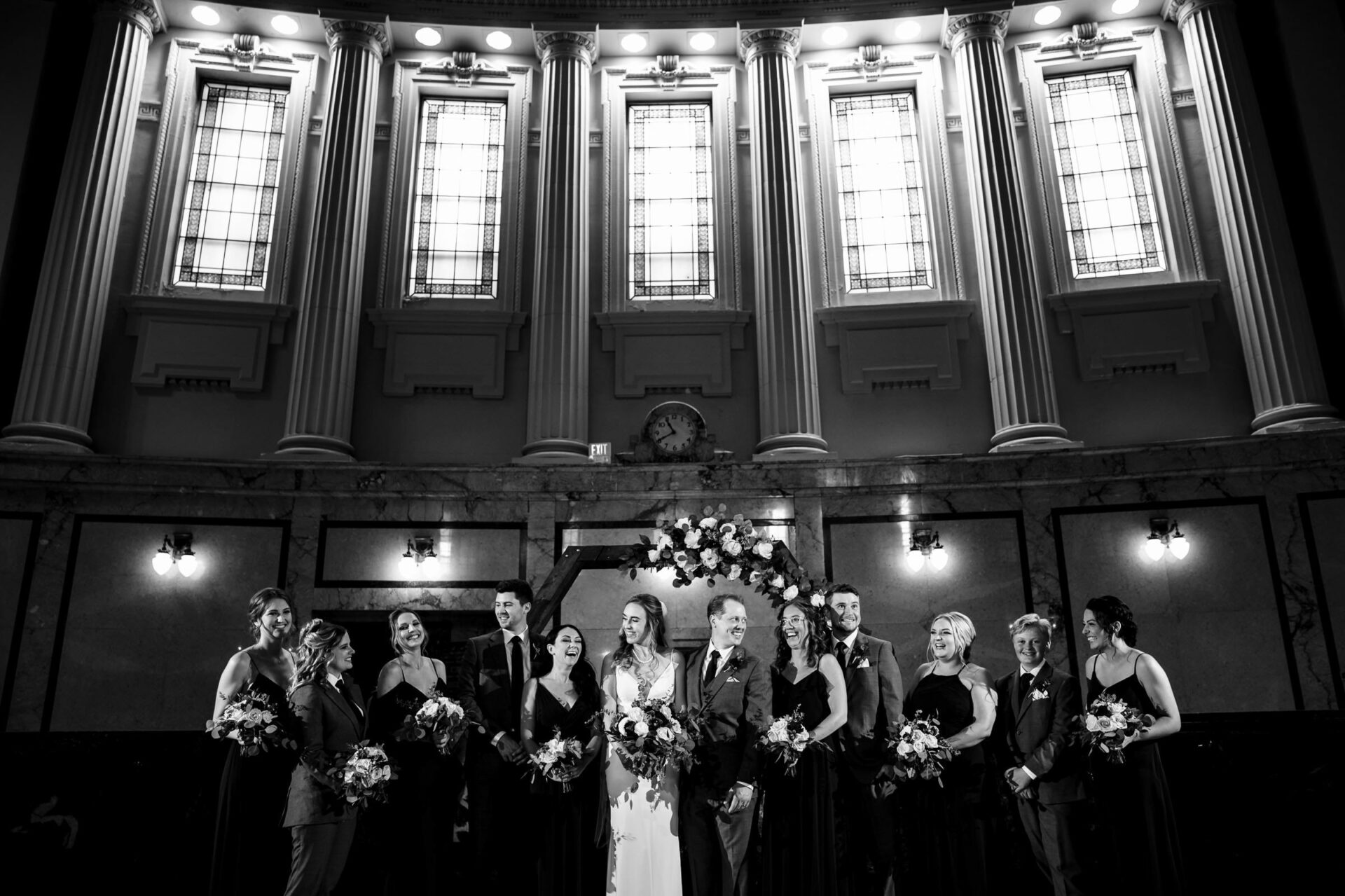 Best Winnipeg Wedding Photos: A wedding party poses in a grand hall with large windows and columns.
