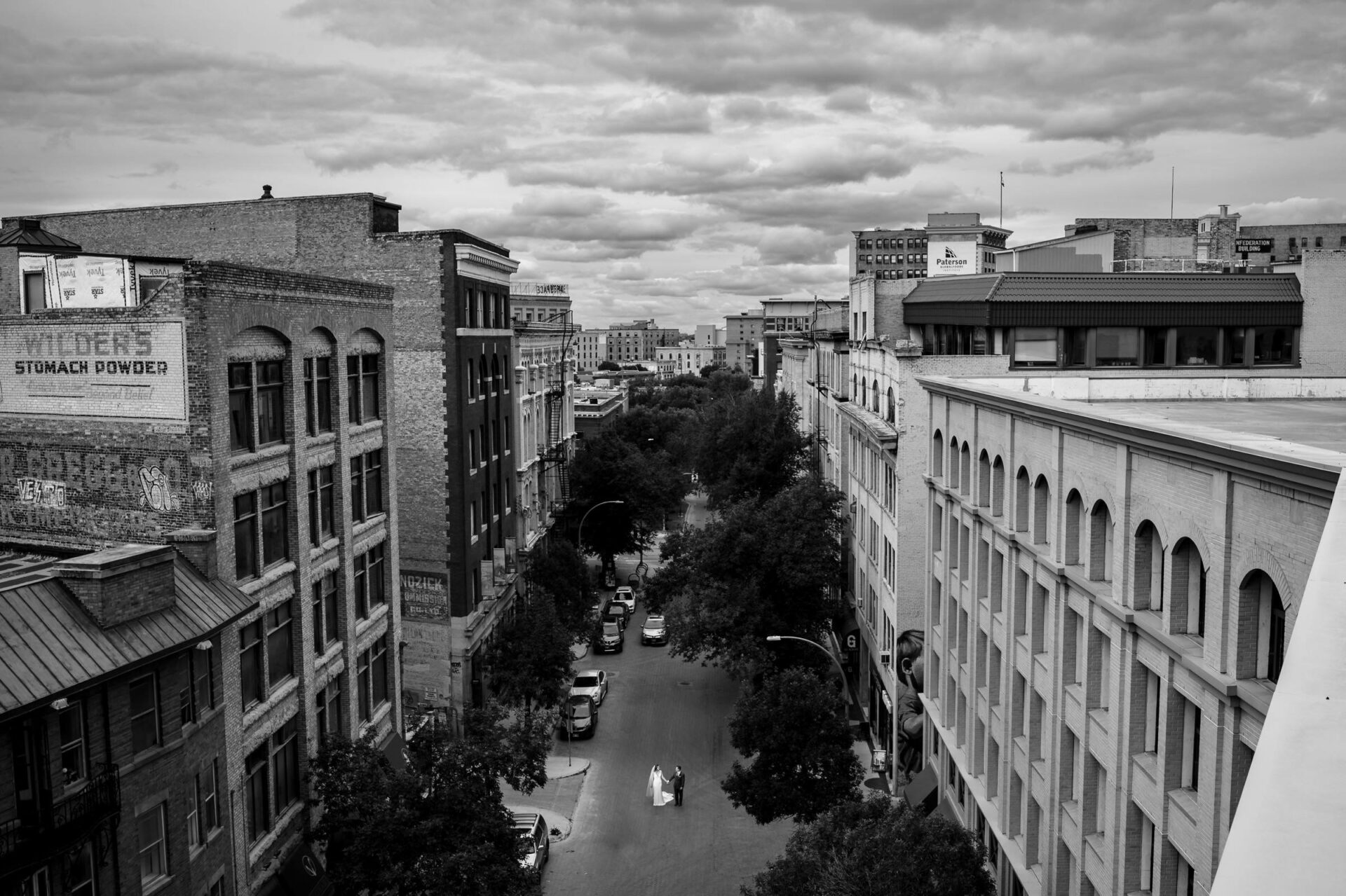 Best Winnipeg wedding photos capture a street between old brick buildings under cloudy skies.