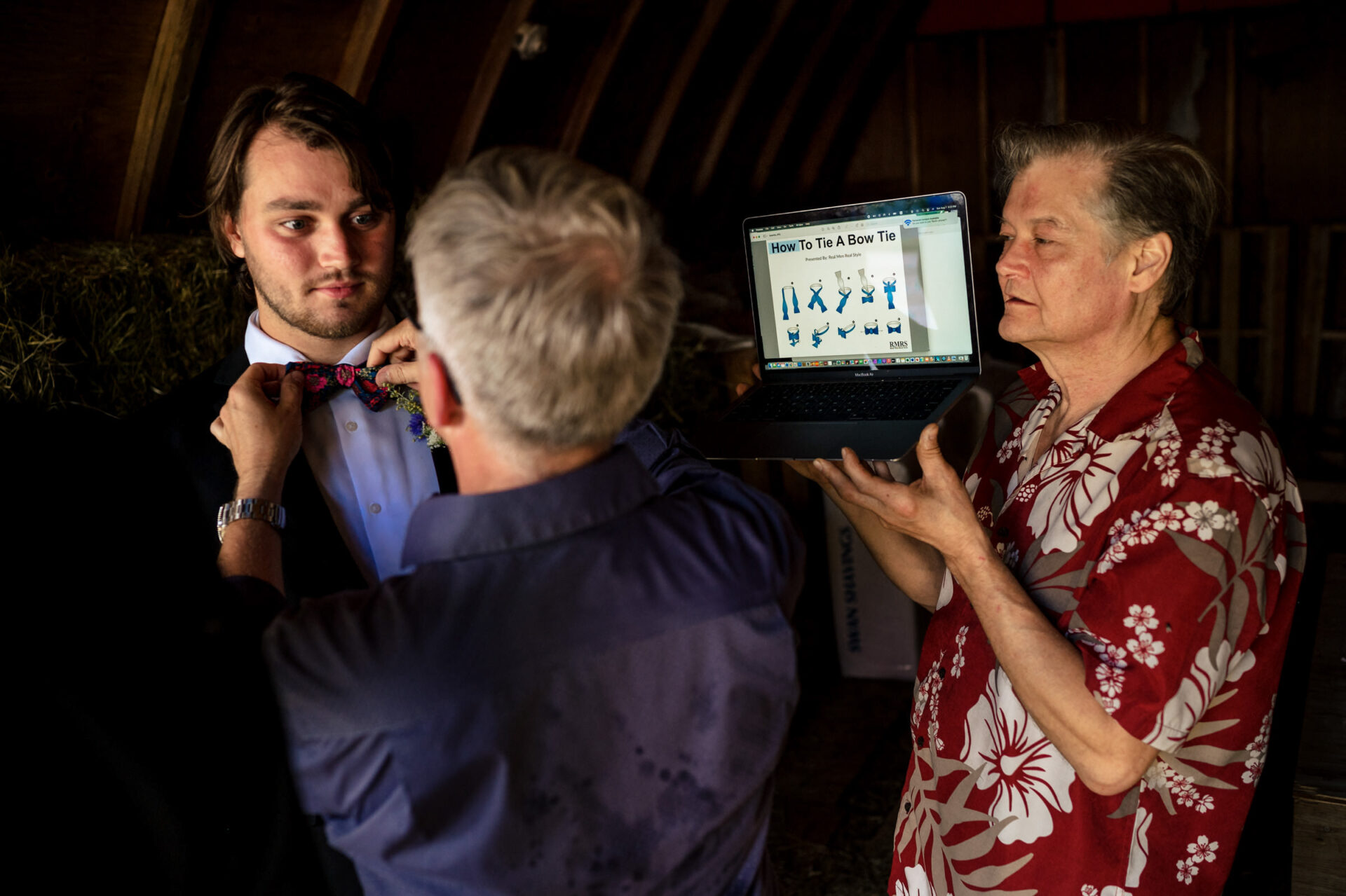 In a rustic room, three men tie bow ties using an online guide—best Winnipeg wedding vibes.