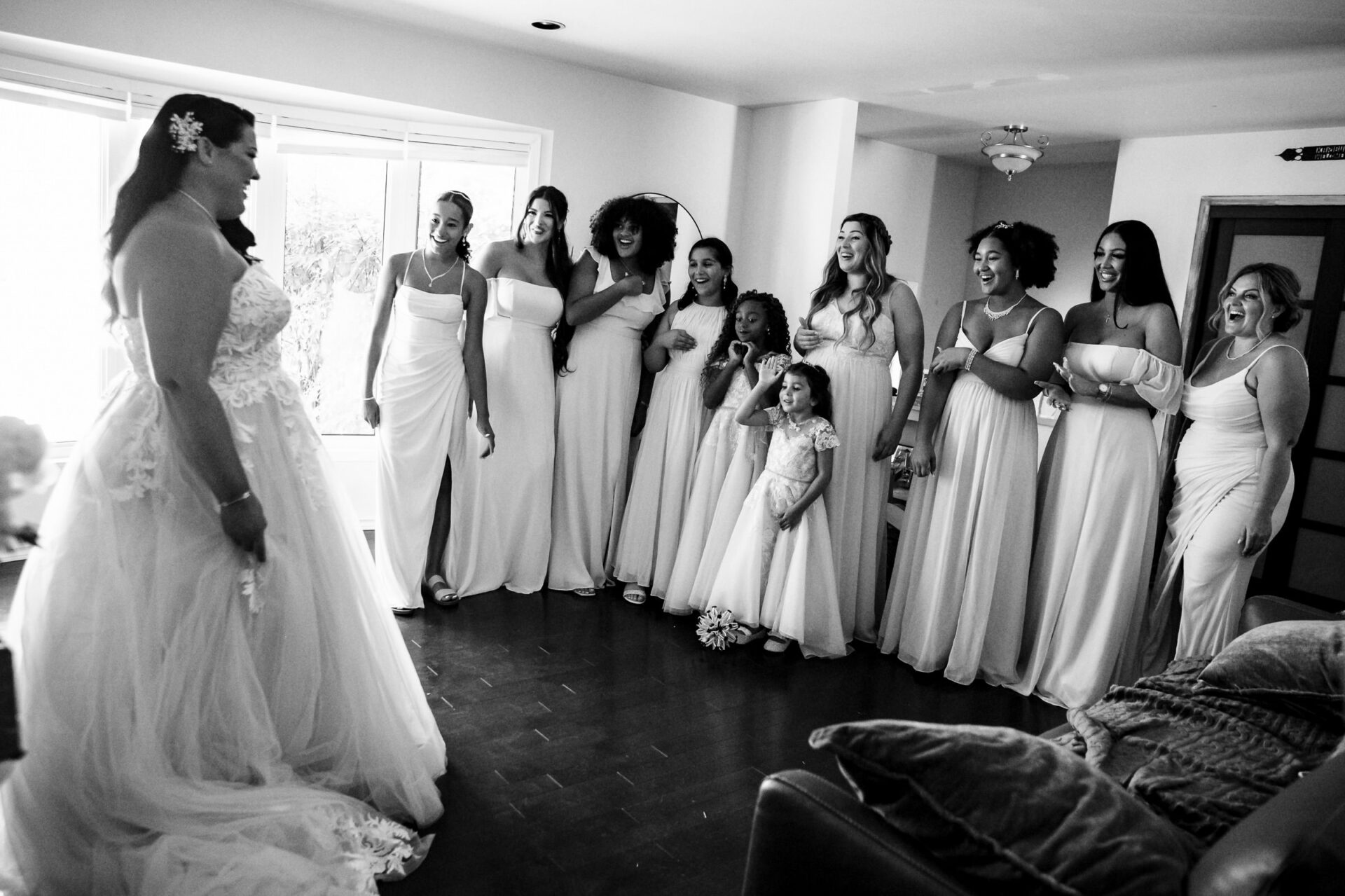 Bride smiling as bridesmaids and a flower girl react excitedly in bright Winnipeg setting.