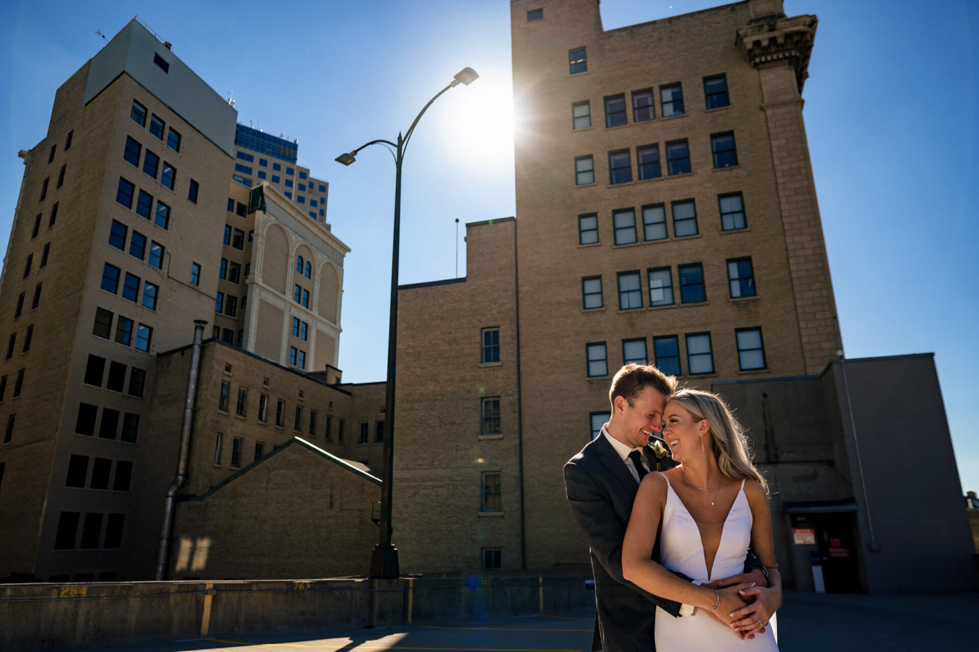 A couple embraces on a sunny rooftop with Winnipeg's skyline as the perfect backdrop.