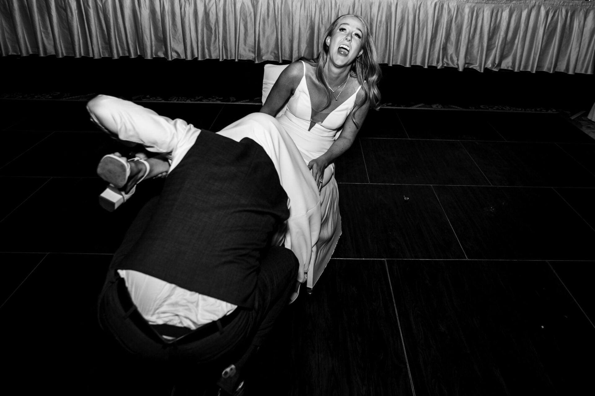 Bride laughs as groom retrieves garter at the Best Winnipeg Wedding Photos reception.