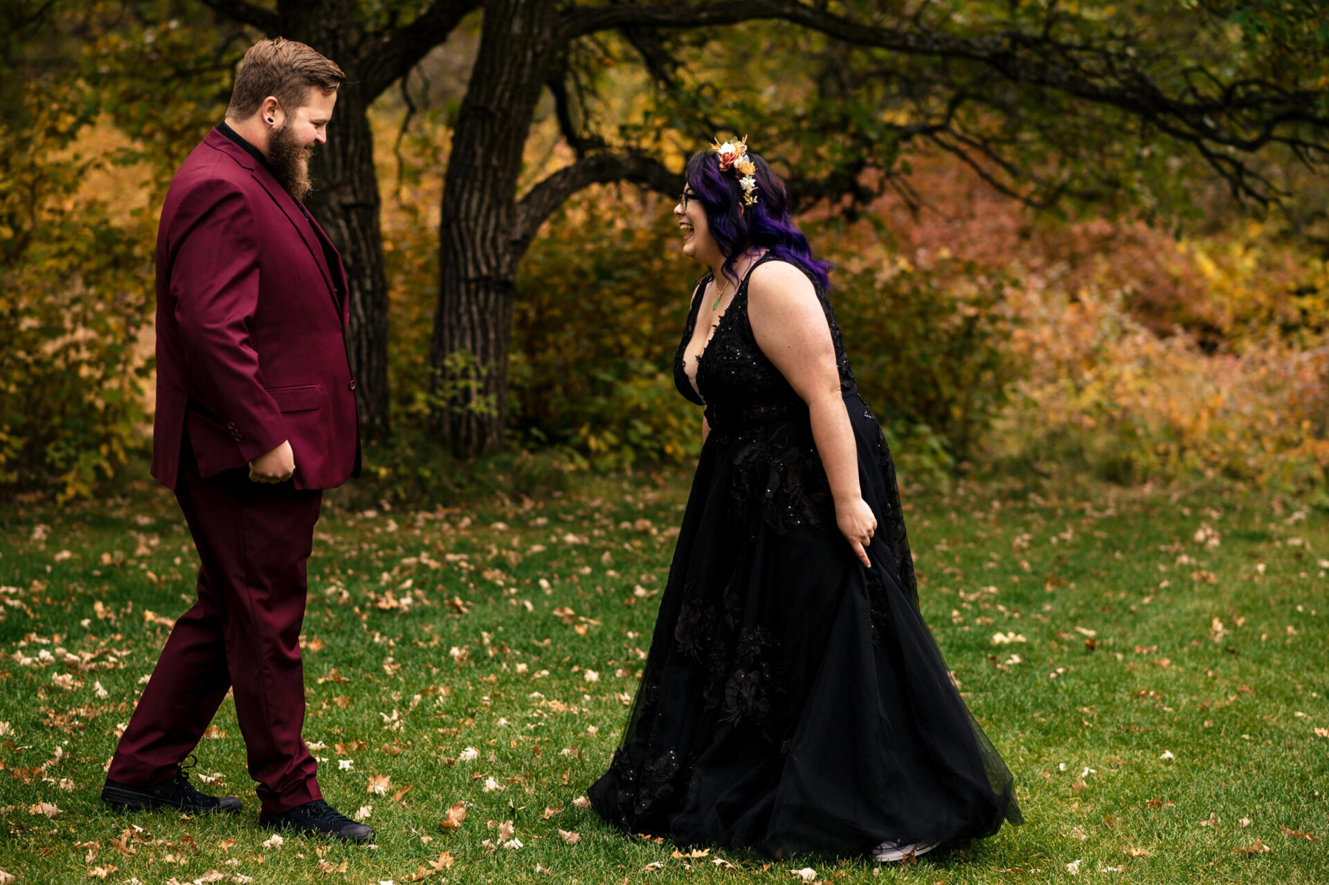 Couple smiling under a tree, she in black dress, he in maroon suit: Best Winnipeg Wedding Photos.
