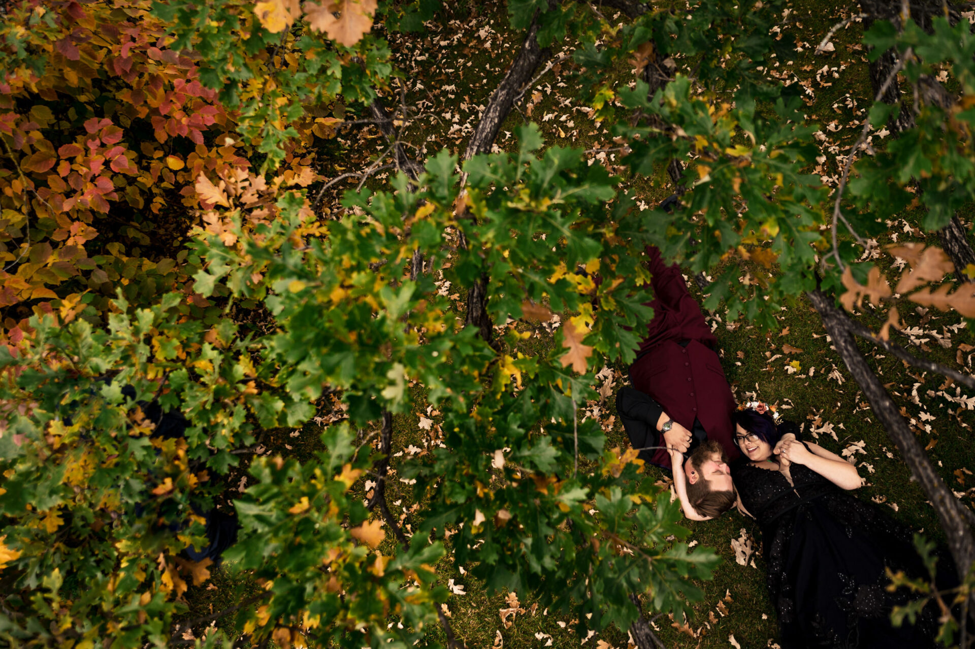 Couple in formal attire lying on grass, framed by autumn leaves—best Winnipeg wedding snapshot.