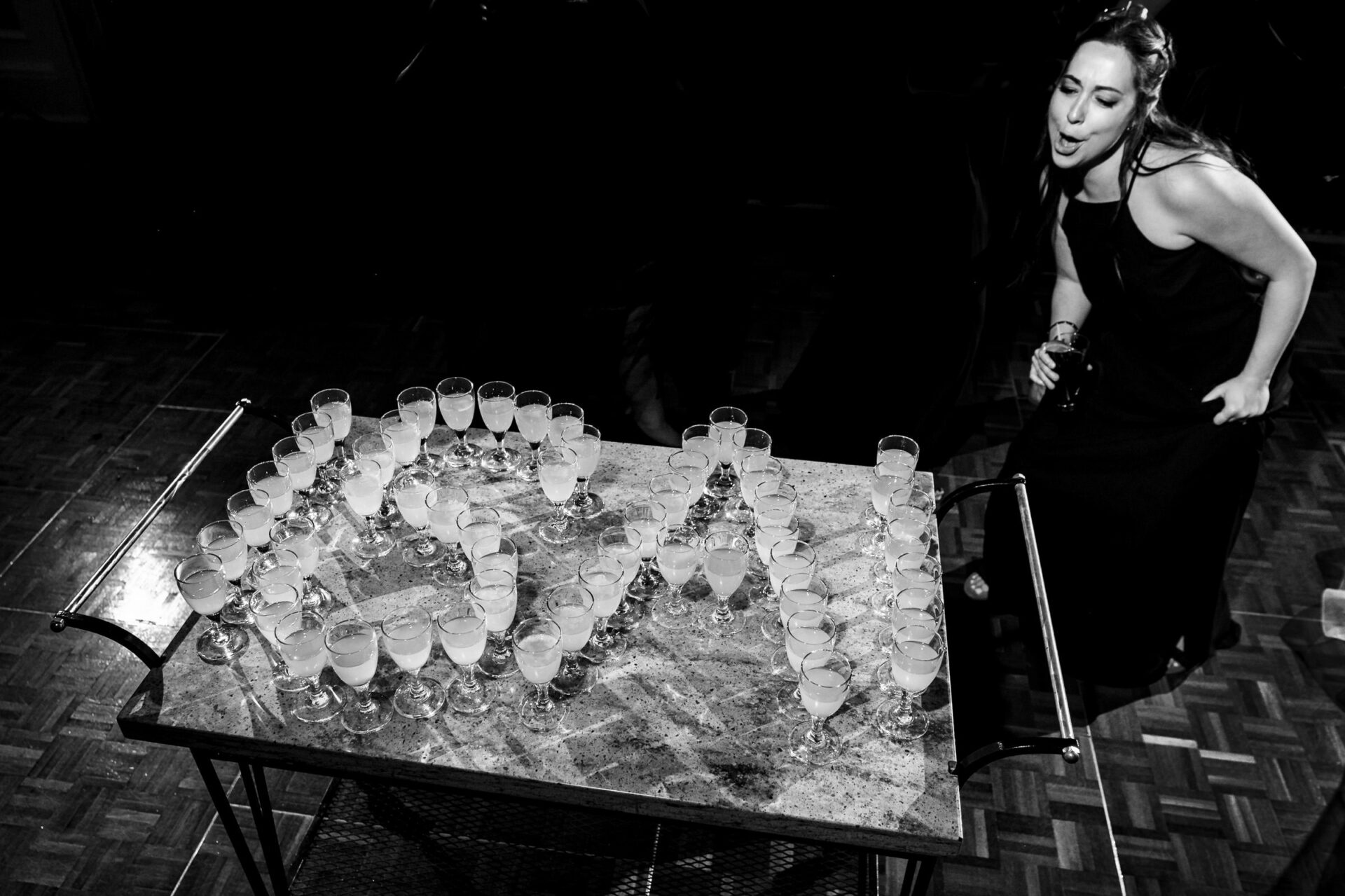 Smiling woman in black dress enjoys glasses spelling "USA" at a wedding.
