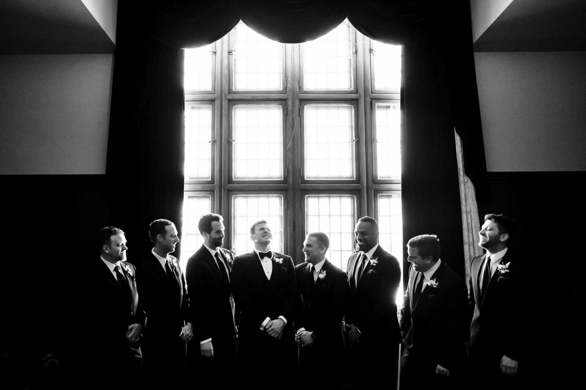 Best Winnipeg Wedding Photos: Groom with groomsmen in suits laughing by a large window.