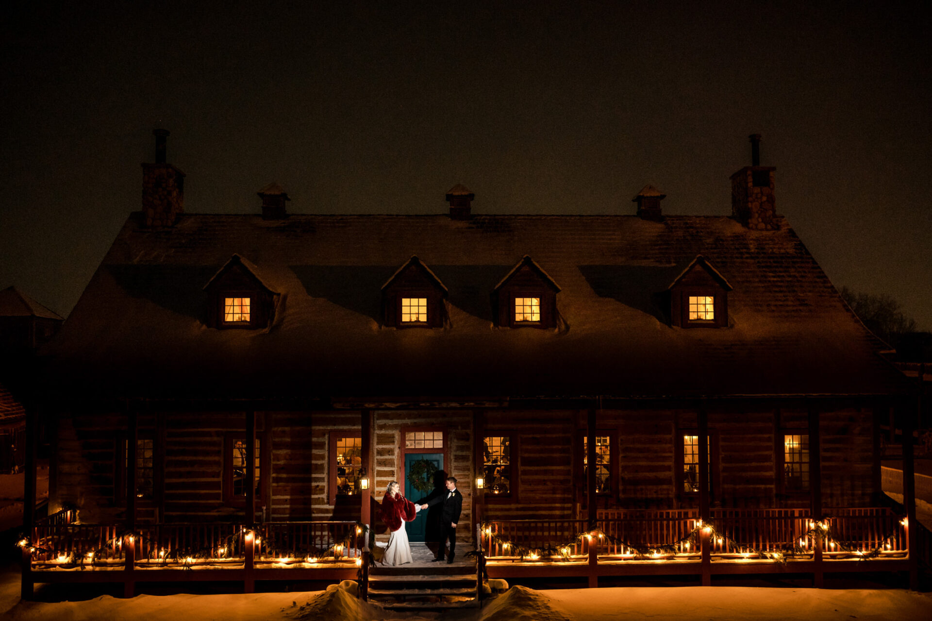 Best Winnipeg wedding photos: A couple outside a lit log cabin, embraced by snowy night.