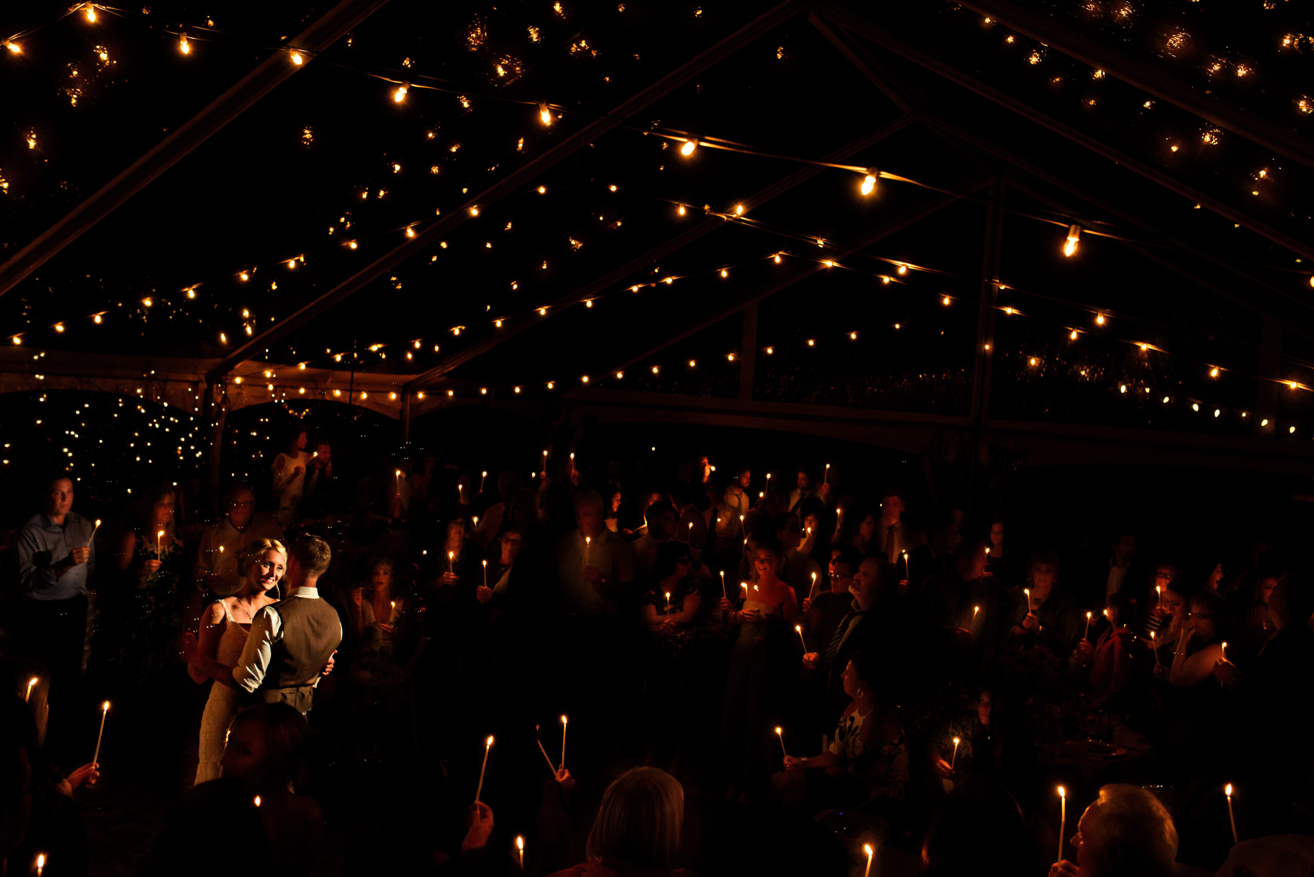A couple dances under string lights; Winnipeg Wedding Photography captures candlelit guests.
