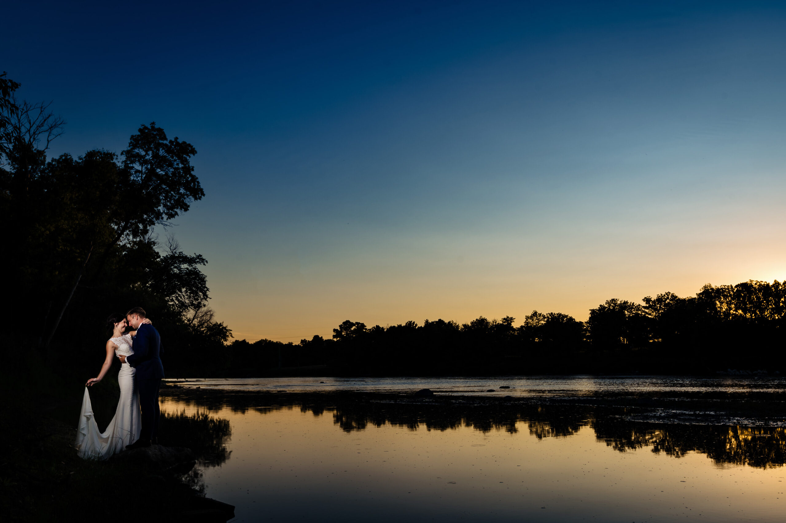 Couple embraces by a tranquil lake at dusk, captured by Winnipeg Wedding Photography.