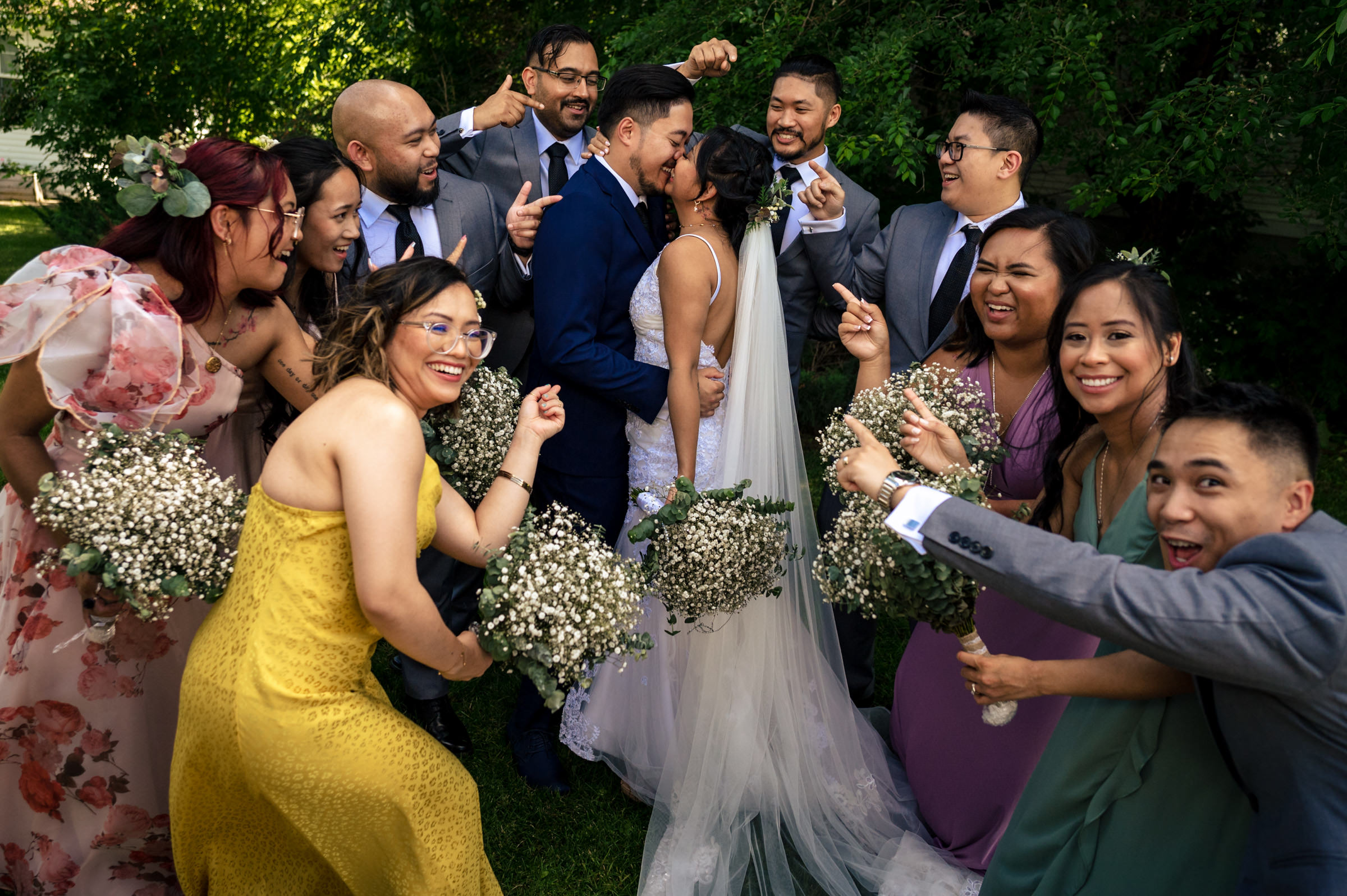 Winnipeg wedding photography captures the cheers as bride and groom kiss amid lush greenery.