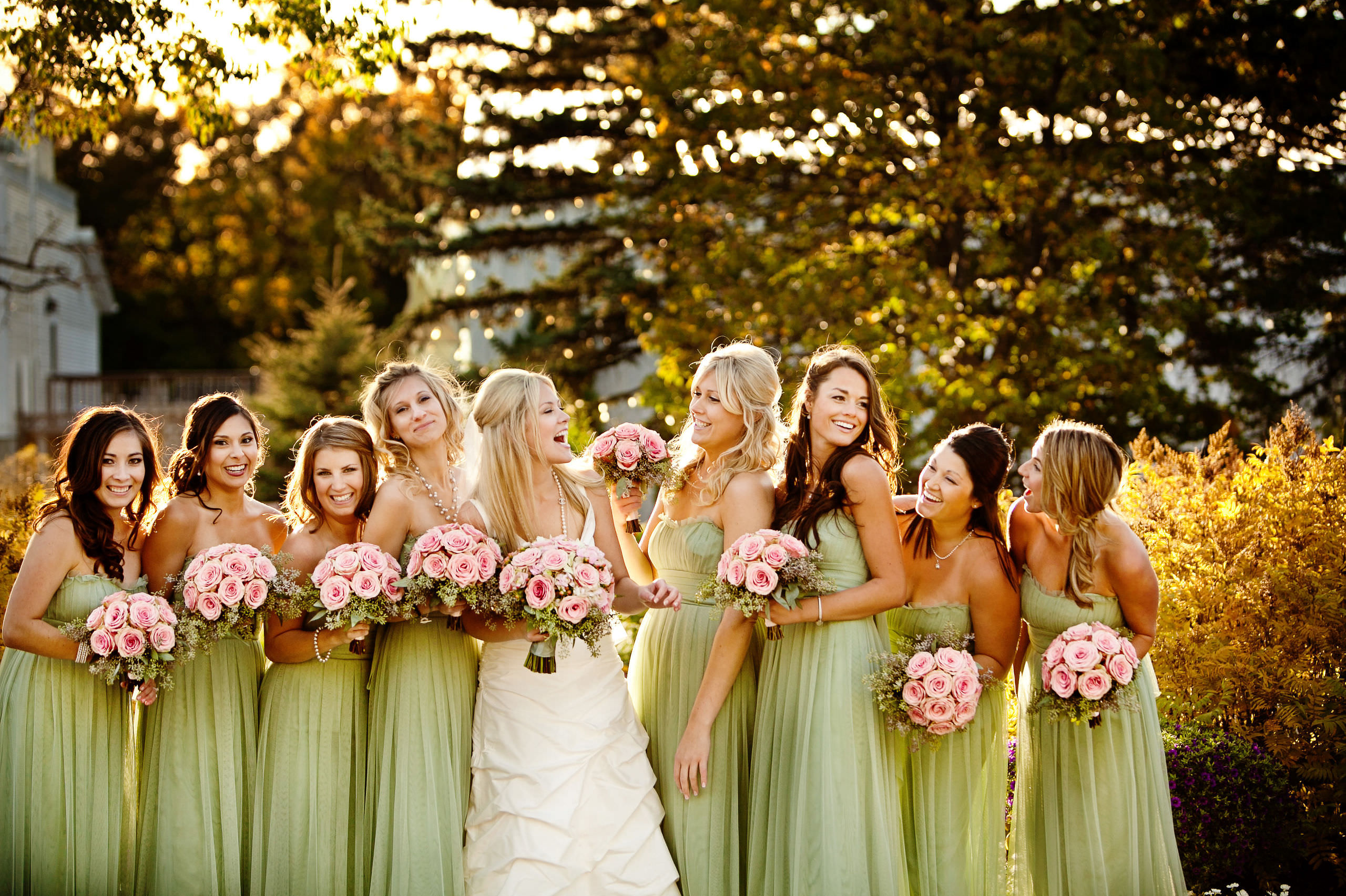 A bride with bridesmaids in green dresses holding pink bouquets, smiling in Winnipeg.