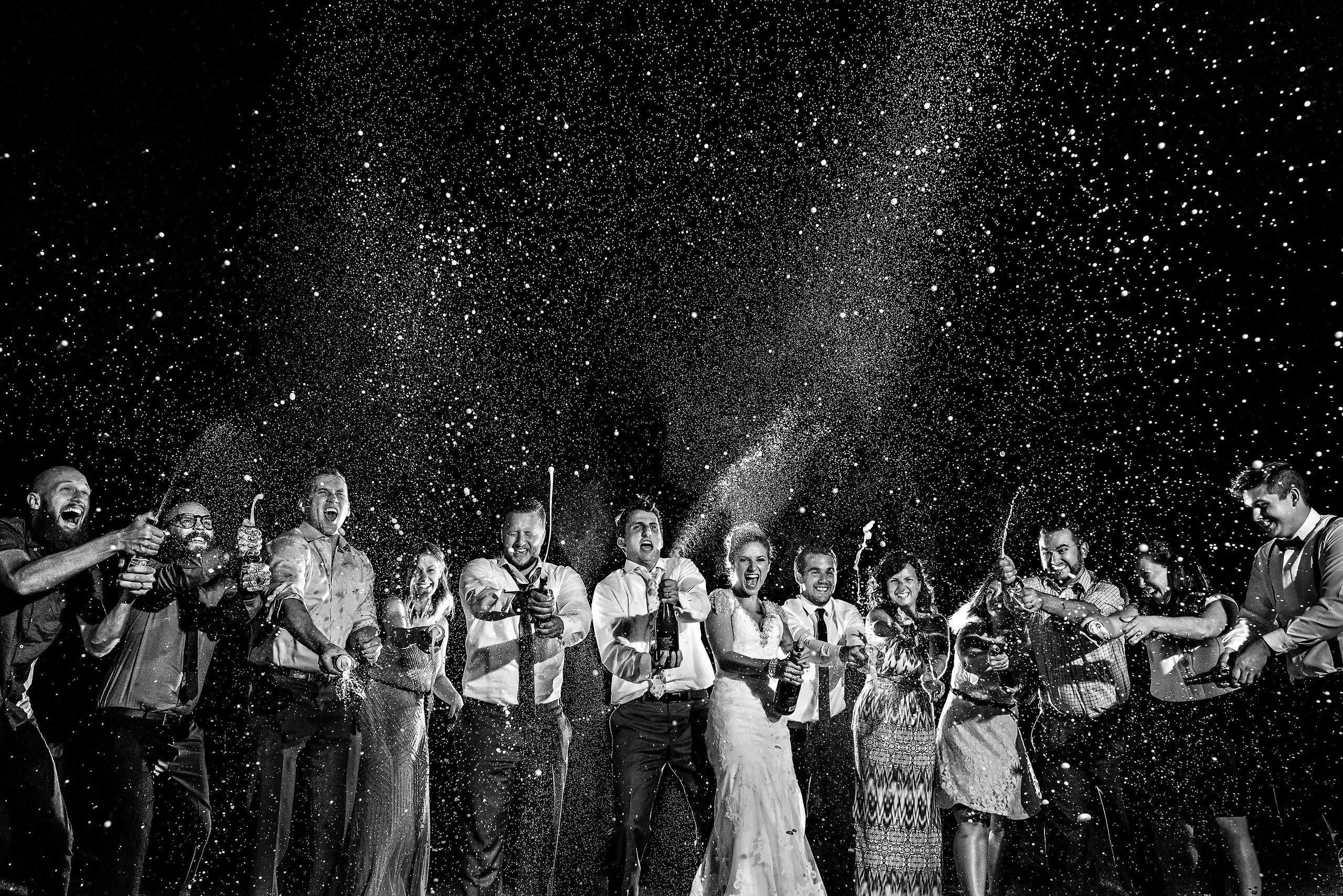 A group celebrates with popping champagne at a Winnipeg wedding, surrounded by sparkling liquid.